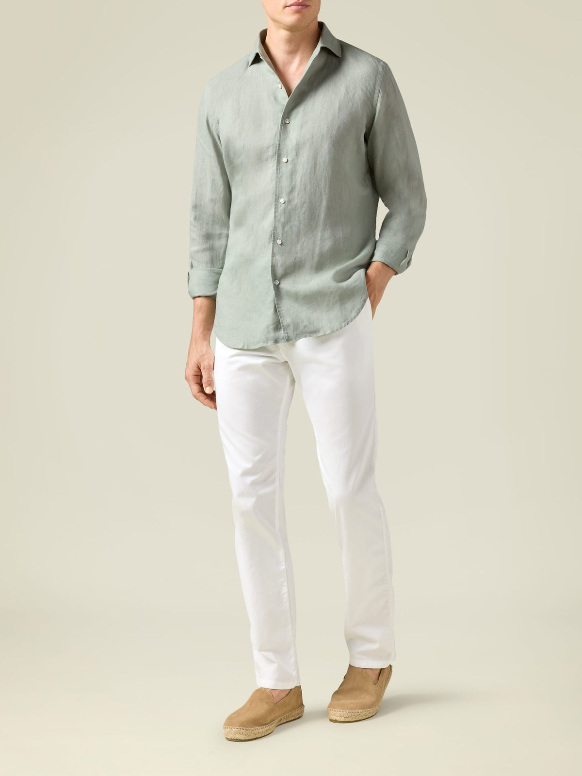 A man models the Lightweight Cotton Chinos in white, styled with a green shirt and tan espadrilles. Full body shot.