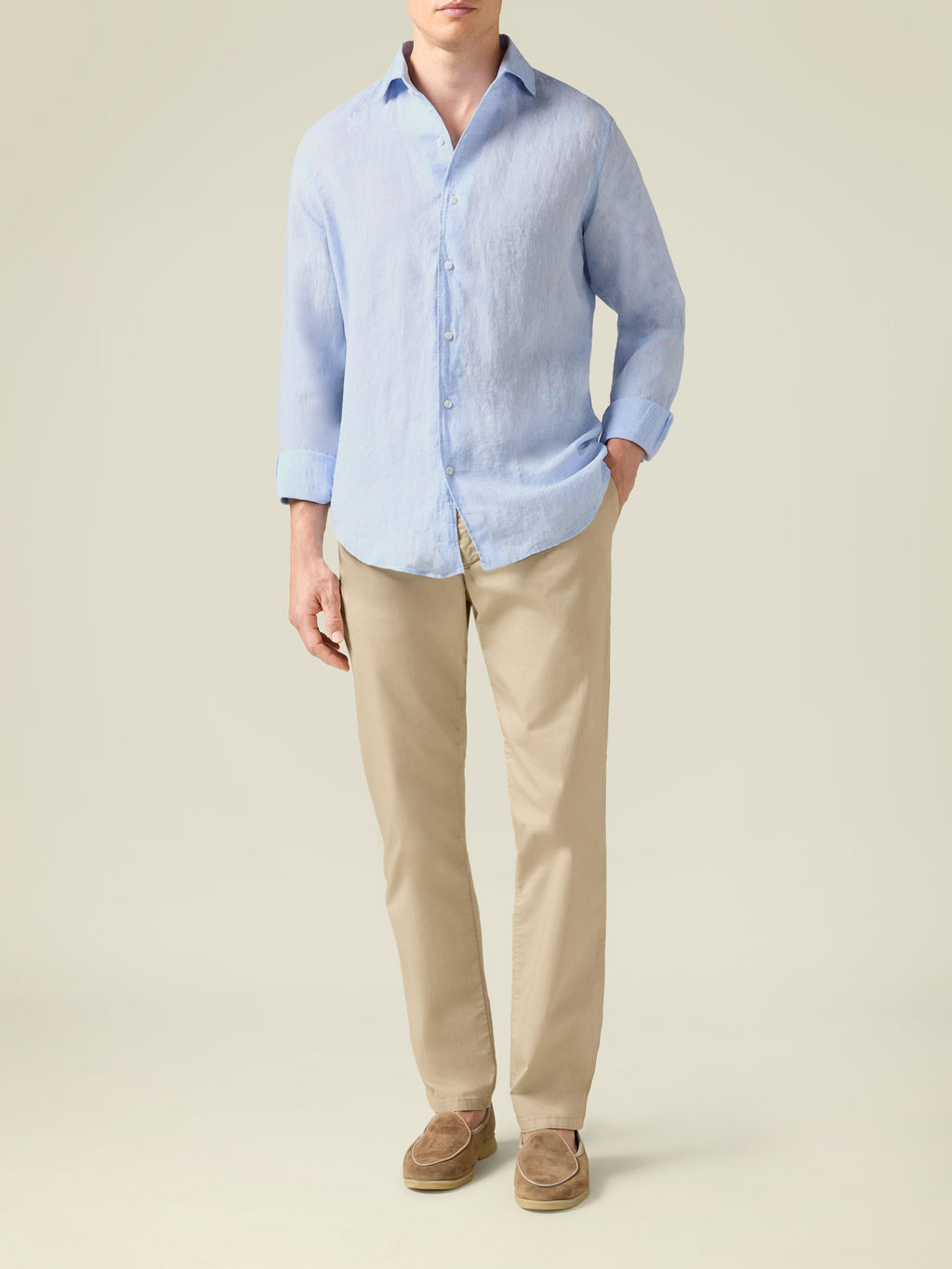 Model wearing cream lightweight cotton chinos, a light blue shirt, and brown suede loafers.