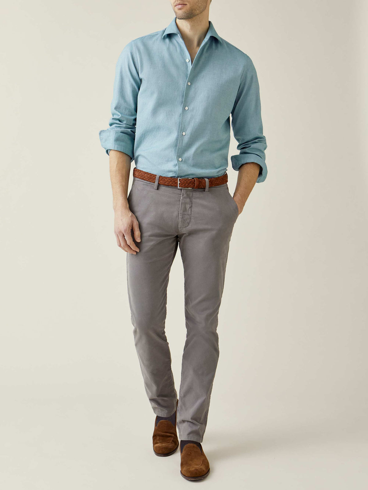 Front view of a model wearing the Elephant Grey Cortina Cotton Chinos with a topaz blue shirt and brown woven belt.