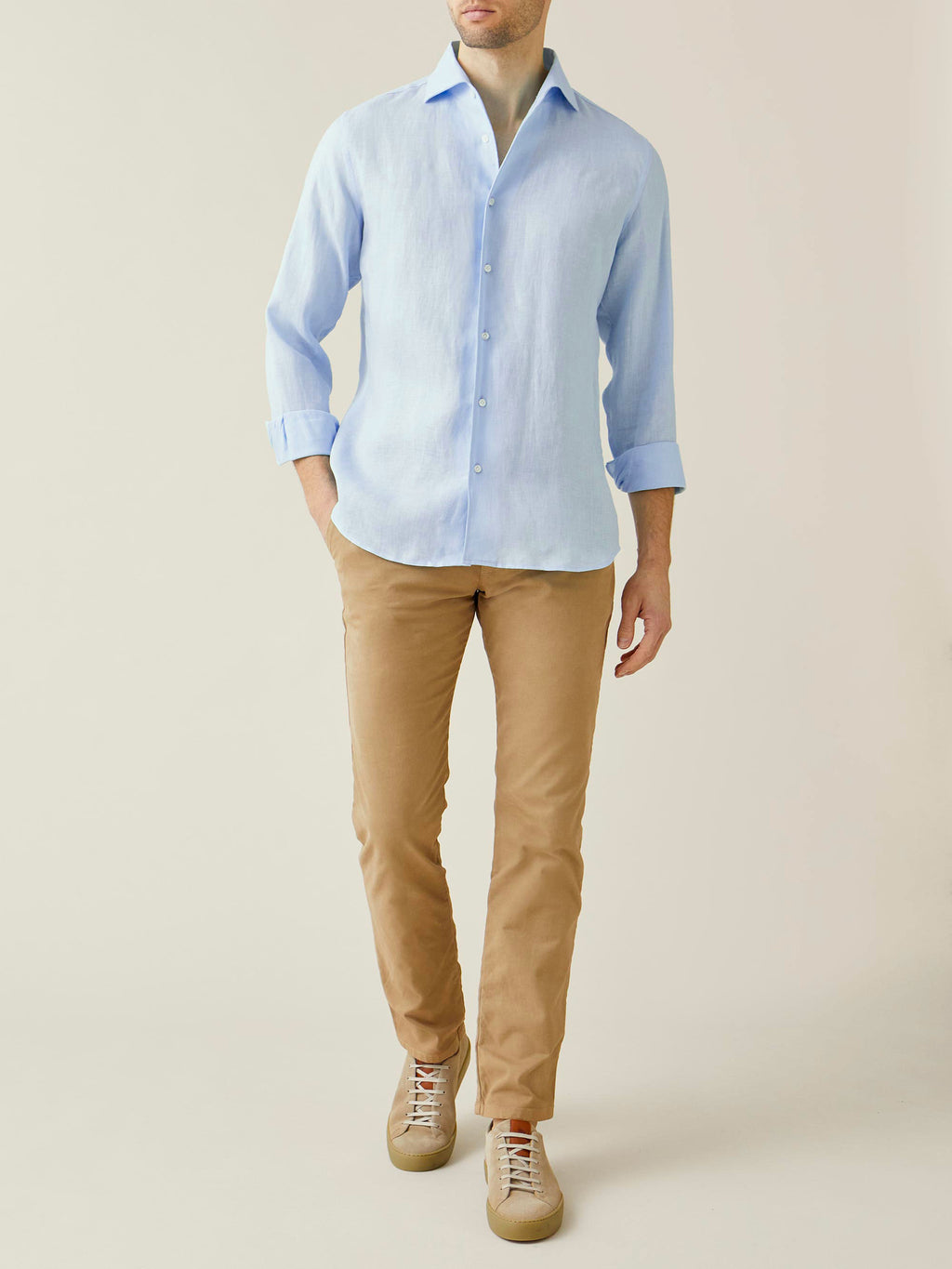 A model wears the Luca Faloni Cortina Cotton Chinos in Camel Beige, styled with a light blue linen shirt and sneakers.