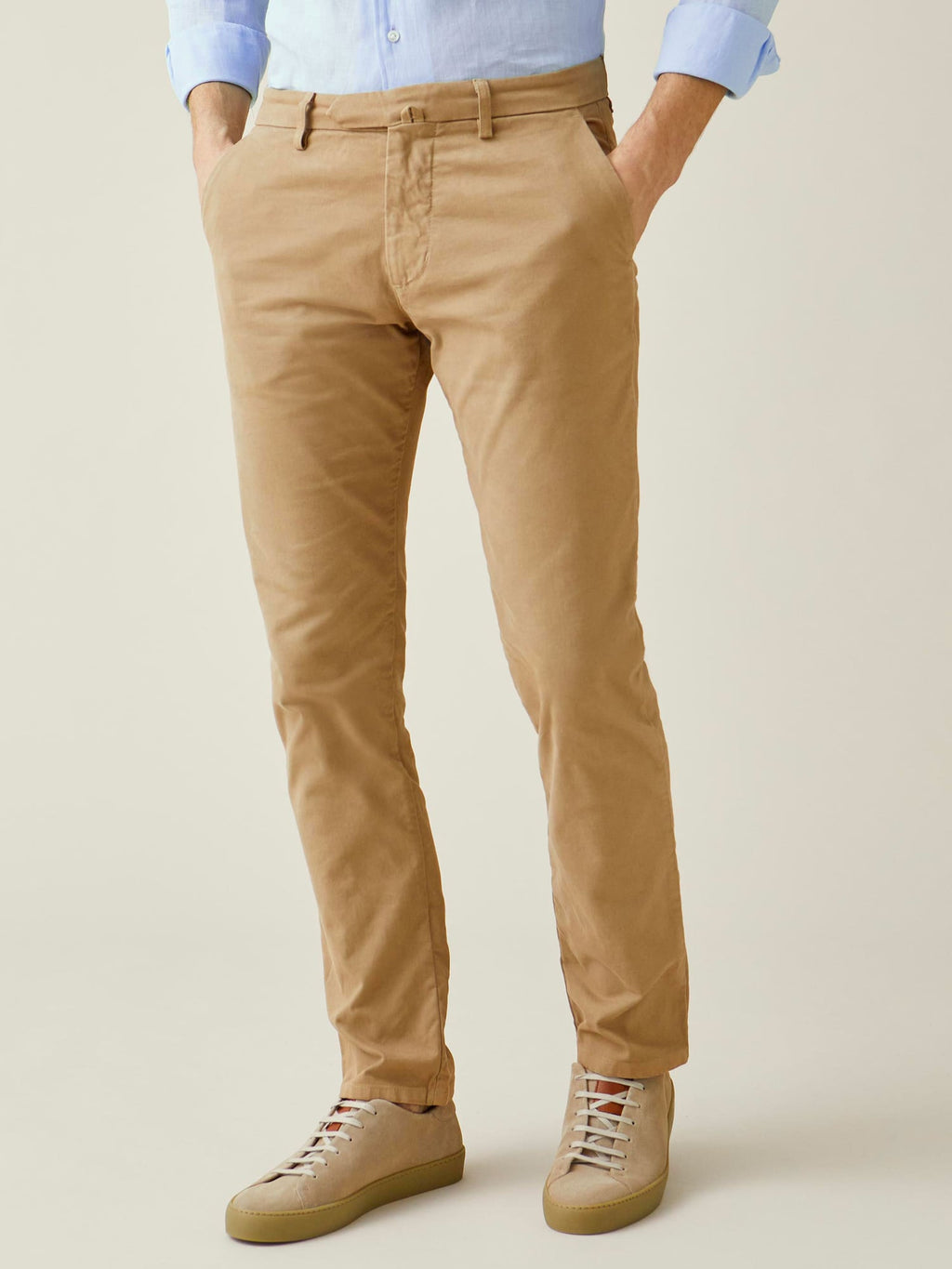 A model wears the Luca Faloni Cortina Cotton Chinos in Camel Beige, paired with a light blue shirt and beige trainers.