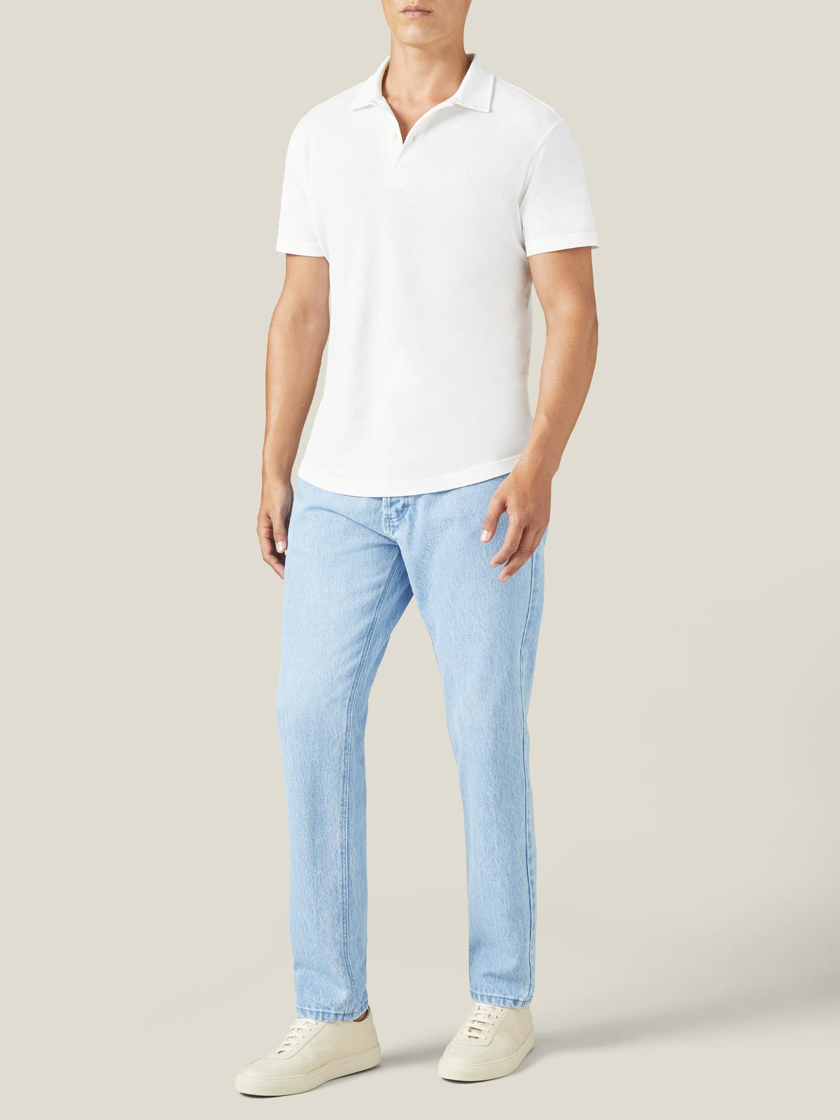 Front view of a man wearing Luca Faloni light blue tapered jeans, styled with a white polo shirt and off-white sneakers.