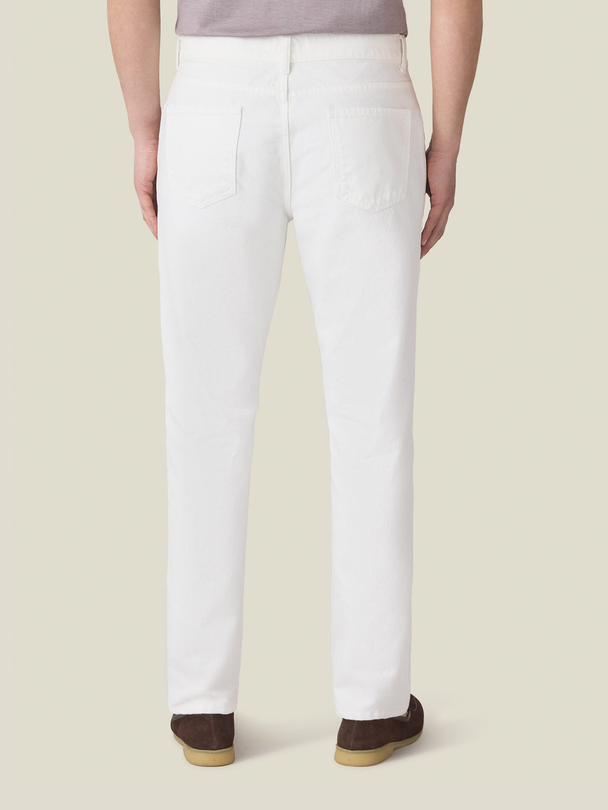 Back view of a model wearing Luca Faloni's white tapered denim jeans, showcasing the fit and rivetless back pockets.