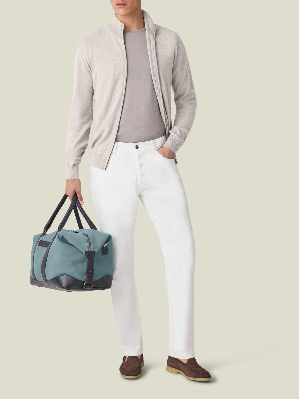 Front view of a model in Luca Faloni's White Jeans, styled with a grey zip cardigan, t-shirt, and a weekender bag.
