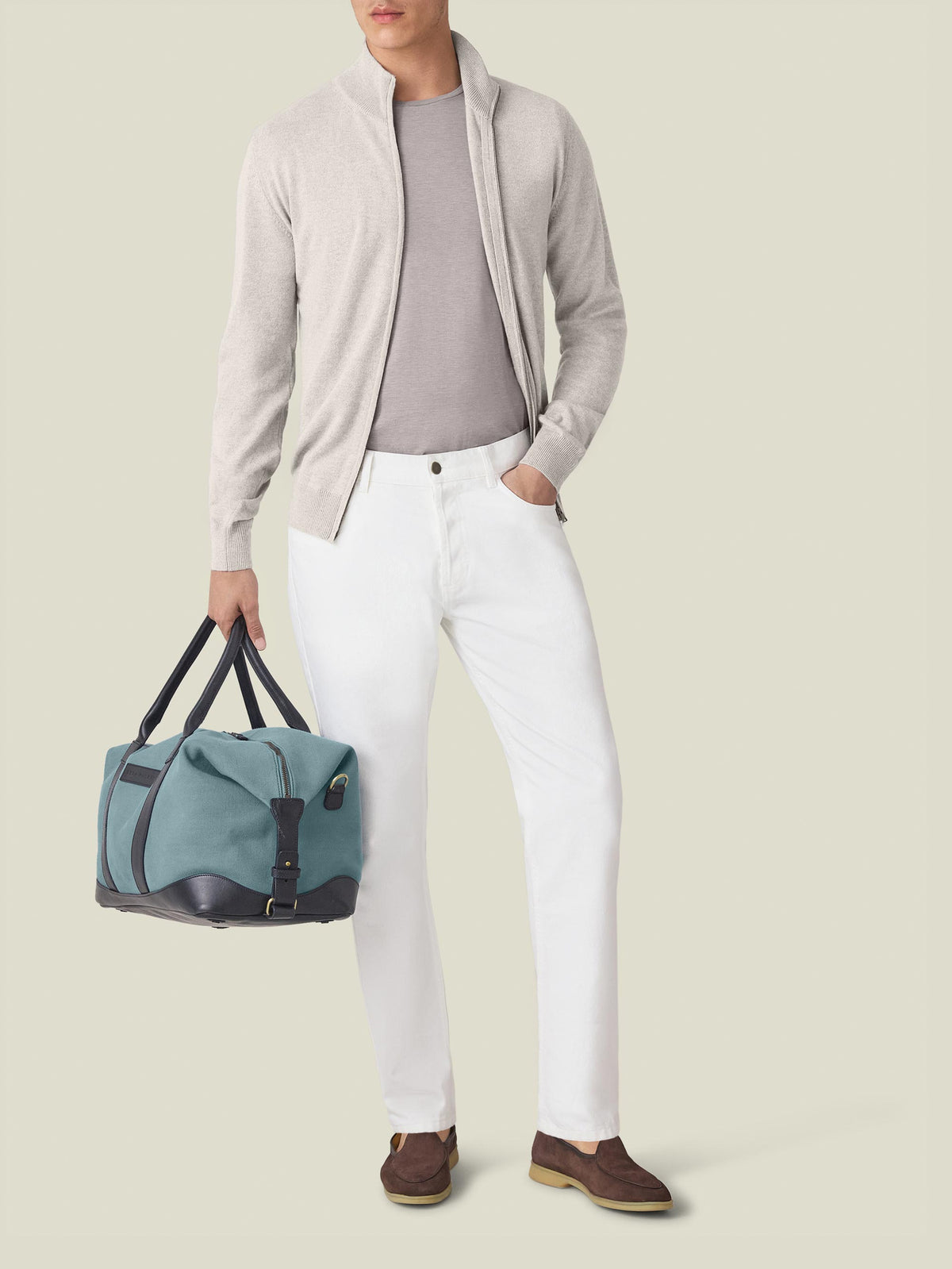 Front view of a model in Luca Faloni's White Jeans, styled with a grey zip cardigan, t-shirt, and a weekender bag.