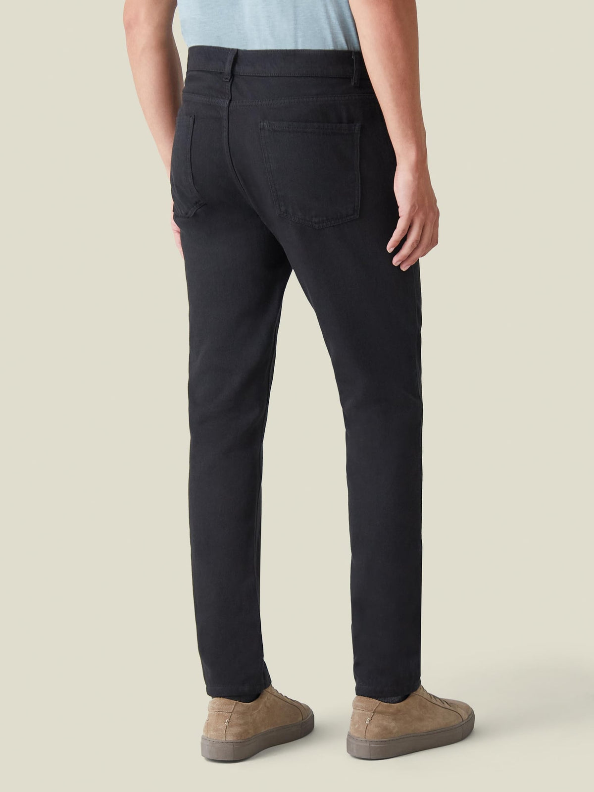 Back view of a model showcasing the tapered fit of Luca Faloni's Black Denim Jeans, styled with tan suede sneakers.