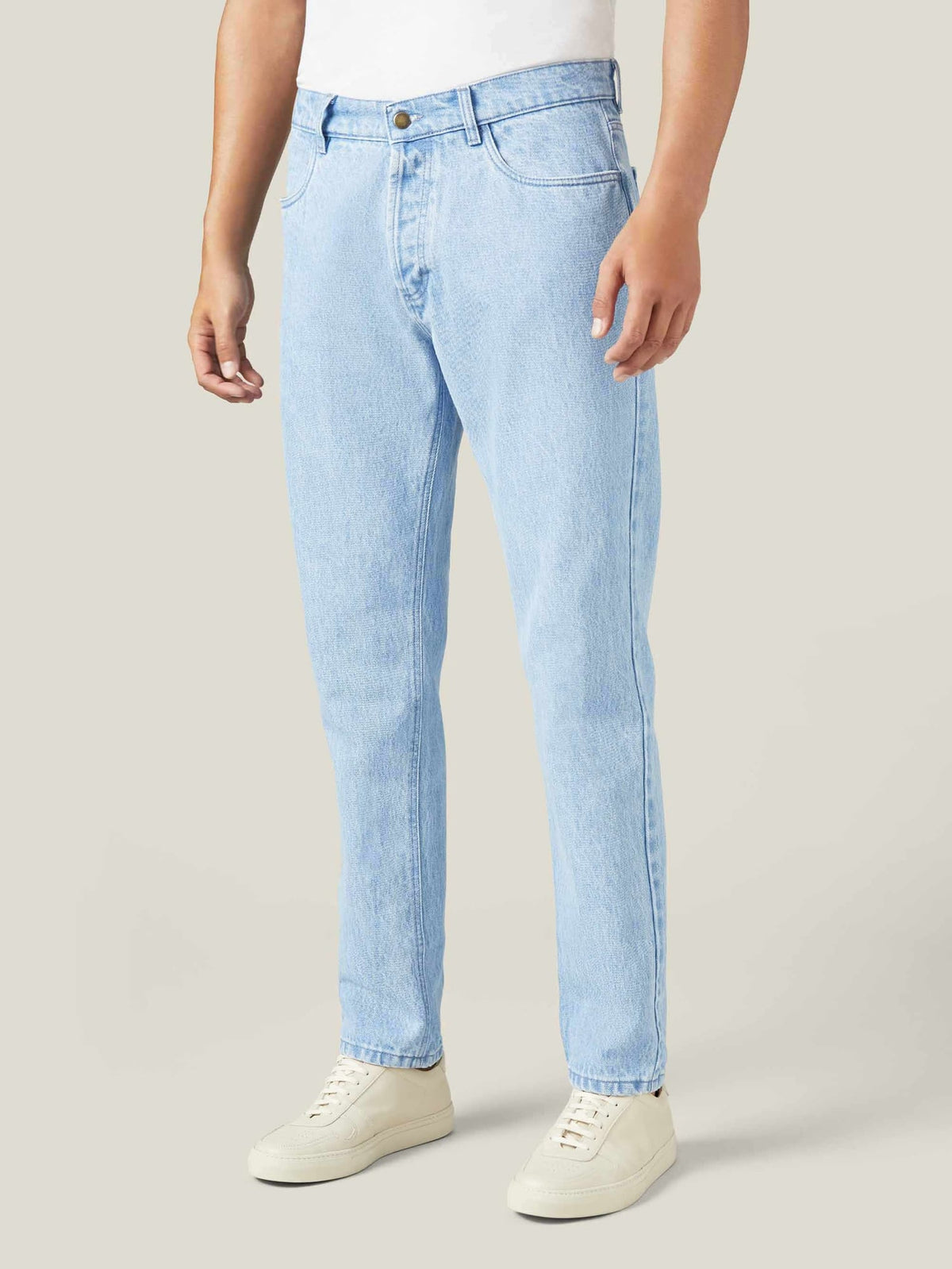A model wears Luca Faloni's light blue tapered jeans, styled with a white t-shirt and off-white sneakers.