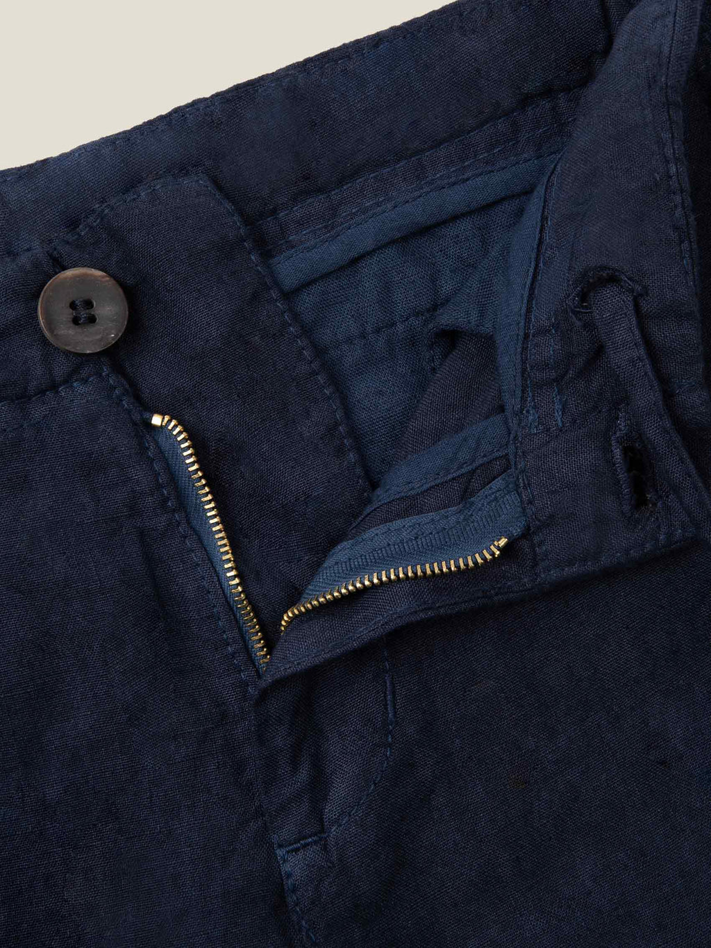 Close-up of the Lipari Junior Linen Trousers in navy blue, showing the horn button, zip, and internal drawstring.