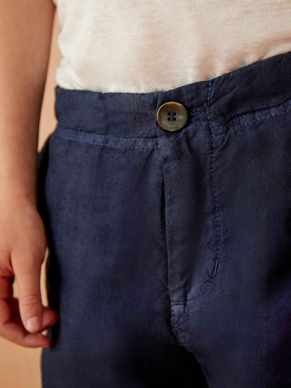 Close-up of the horn button and waistband of the Lipari Junior Linen Trousers in navy blue.