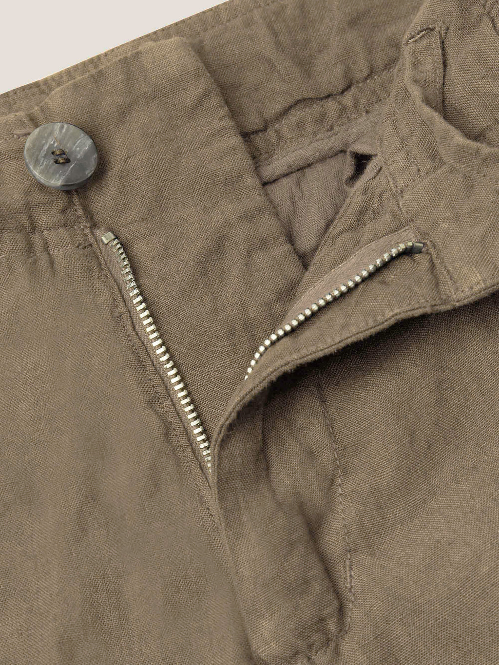Detail shot of the Lipari Linen Trousers in hazelnut brown, focusing on the horn button and zip fly.