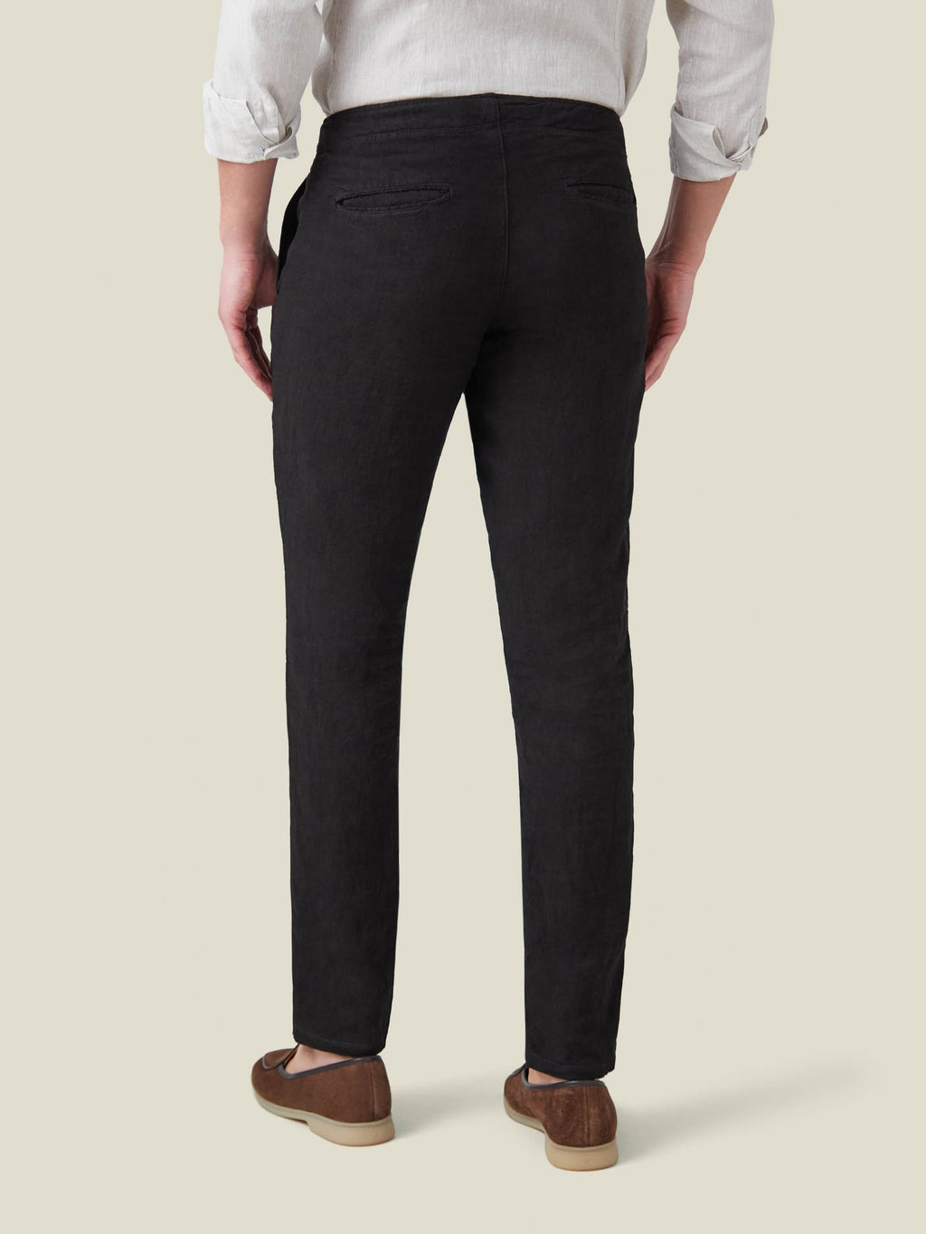 Back view of a model wearing the Lipari Linen Trousers in black, paired with a light shirt and brown loafers.