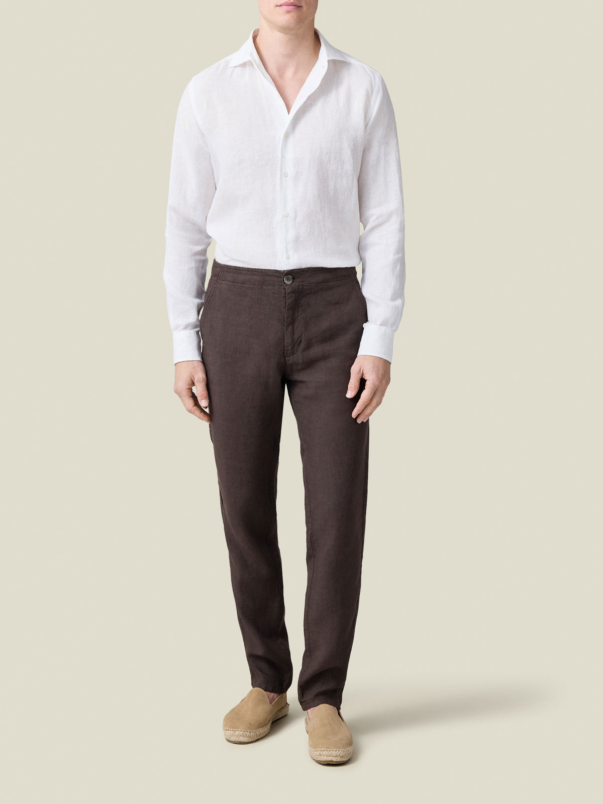 A man models Luca Faloni's Chocolate Brown Lipari Linen Trousers with a white linen shirt and beige espadrilles.
