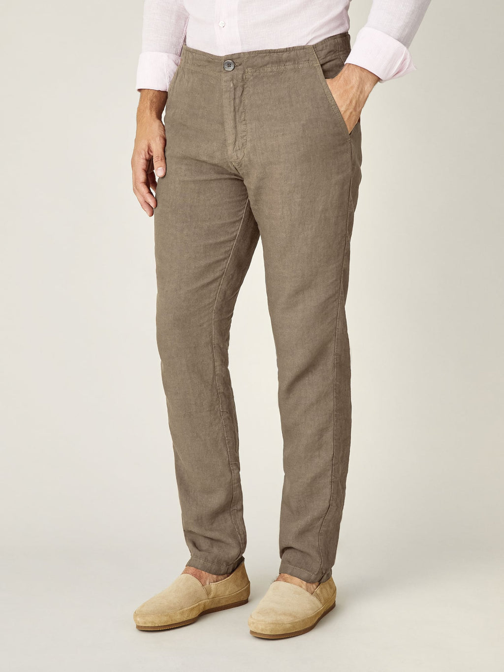 Side view of a man wearing the Lipari Linen Trousers in hazelnut brown, paired with a pink shirt and beige espadrilles.