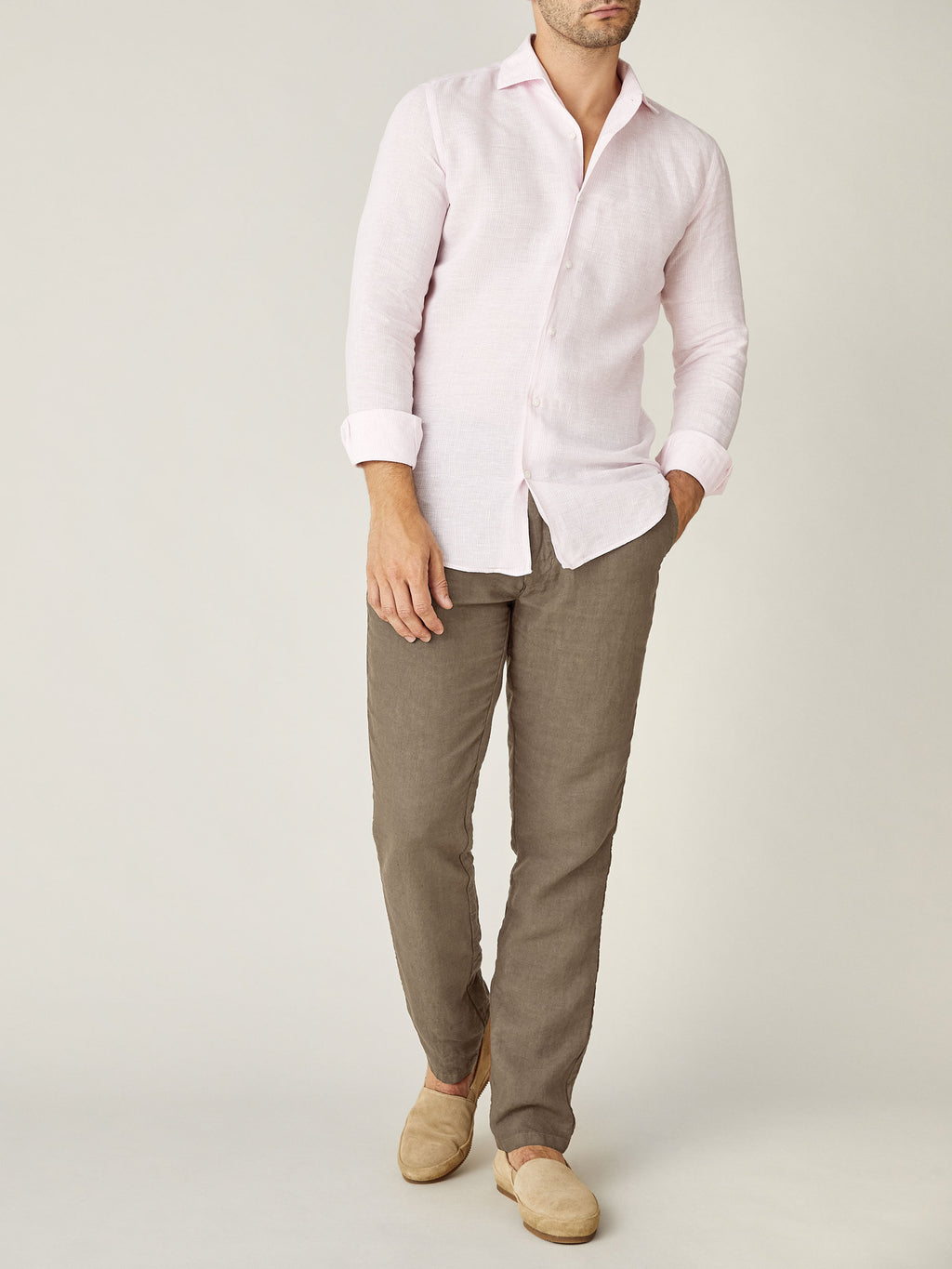 Model wears the Lipari Linen Trousers in Hazelnut Brown, styled with a pink linen shirt and beige slip-on shoes.
