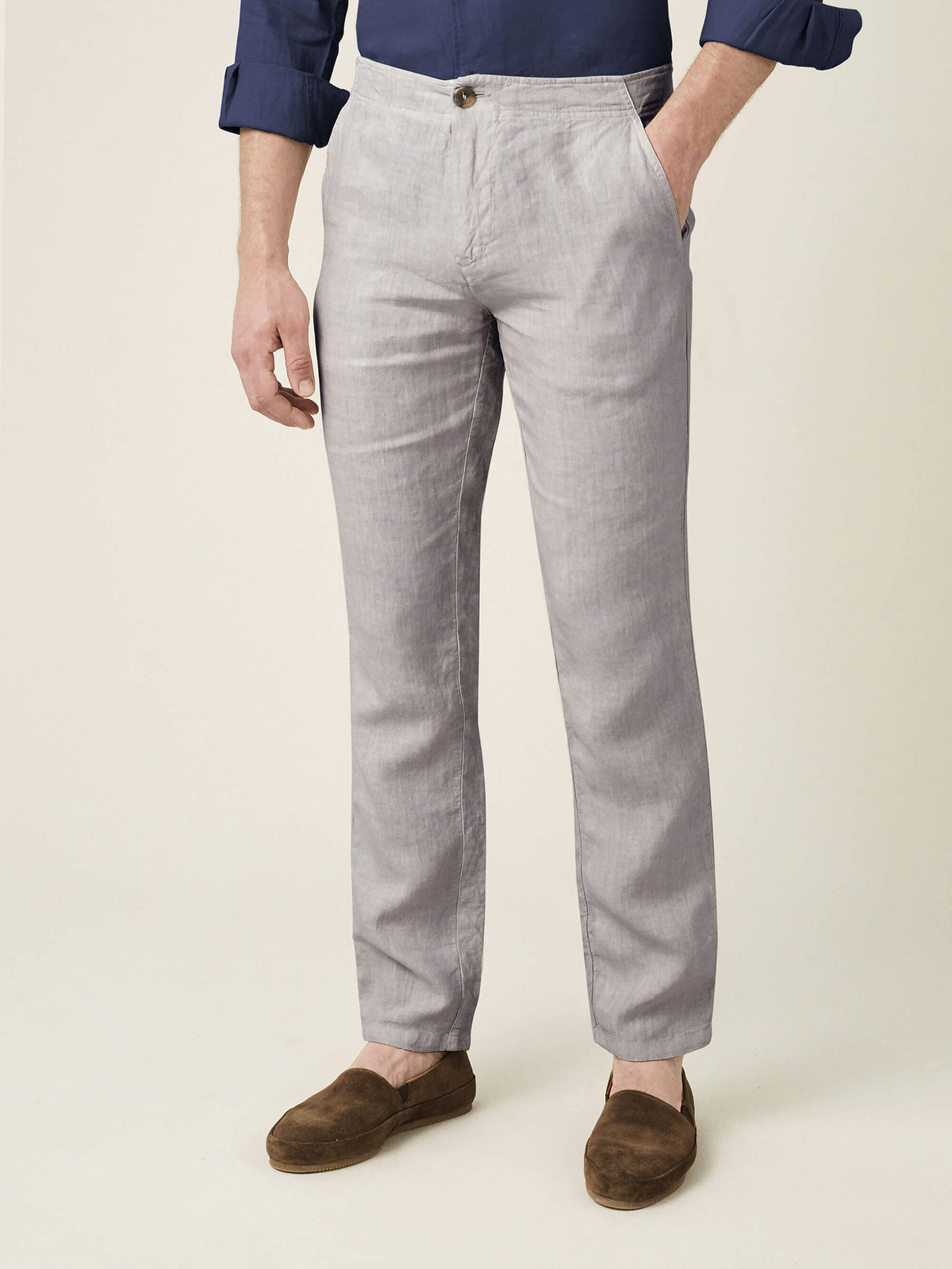 Front view of a man wearing light grey Lipari linen trousers, styled with a navy shirt and brown loafers.