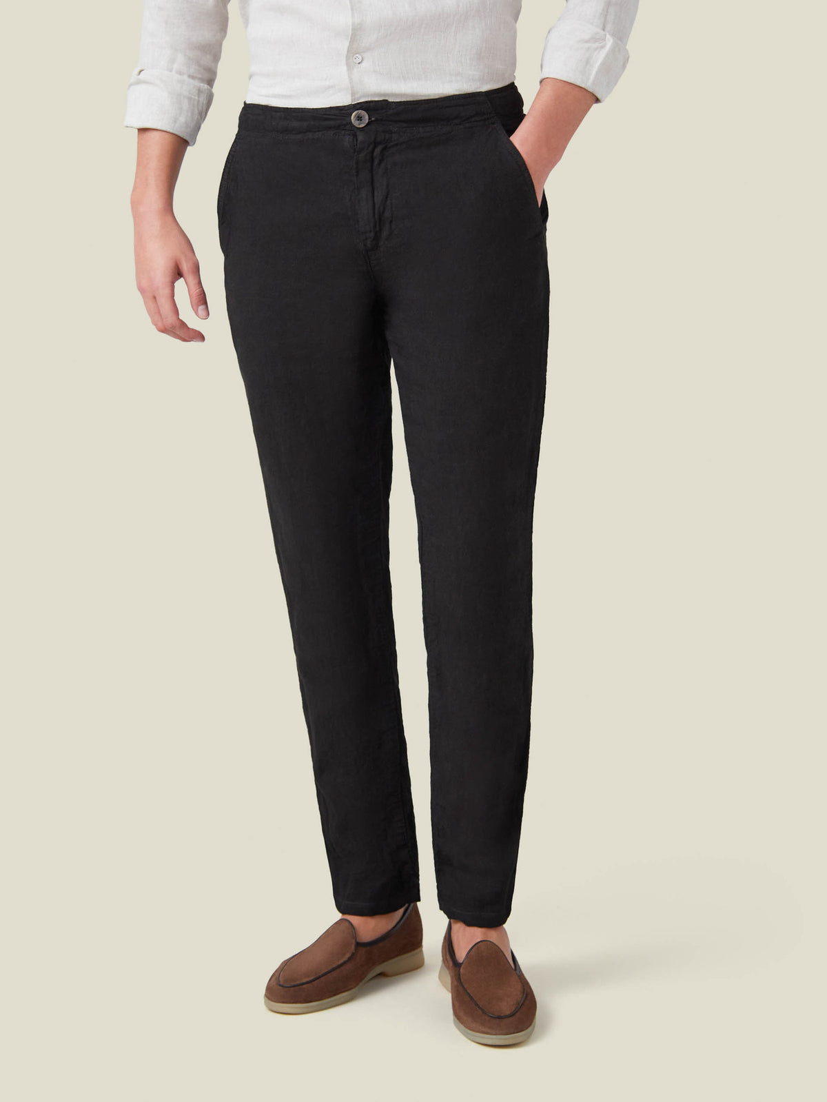A model wears the Lipari Linen Trousers in black, paired with a white linen shirt and brown suede loafers.
