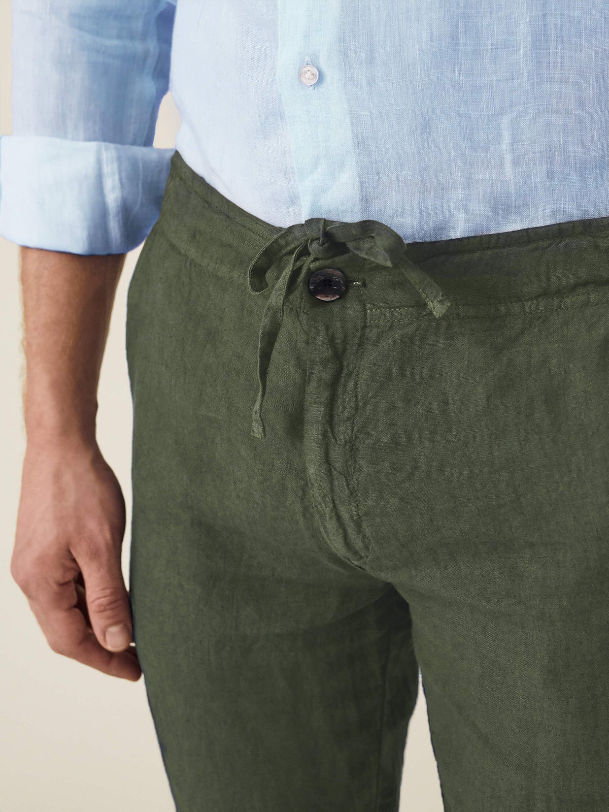 A close-up of the Khaki Green Lipari Linen Trousers, showing the drawstring waist, horn button, and textured fabric.
