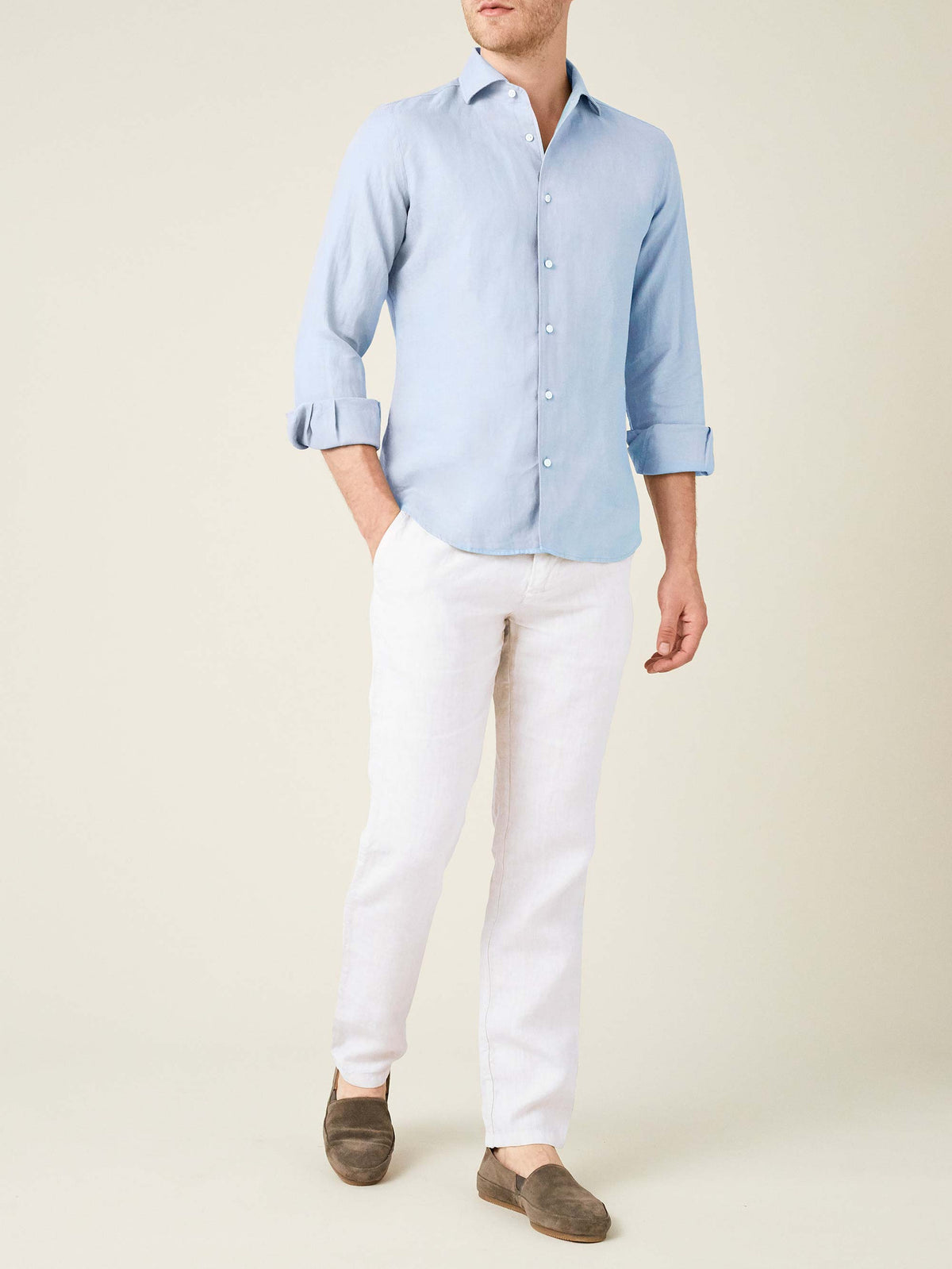 Model wears white Lipari linen trousers, made in Italy, with a light blue shirt and brown suede loafers.