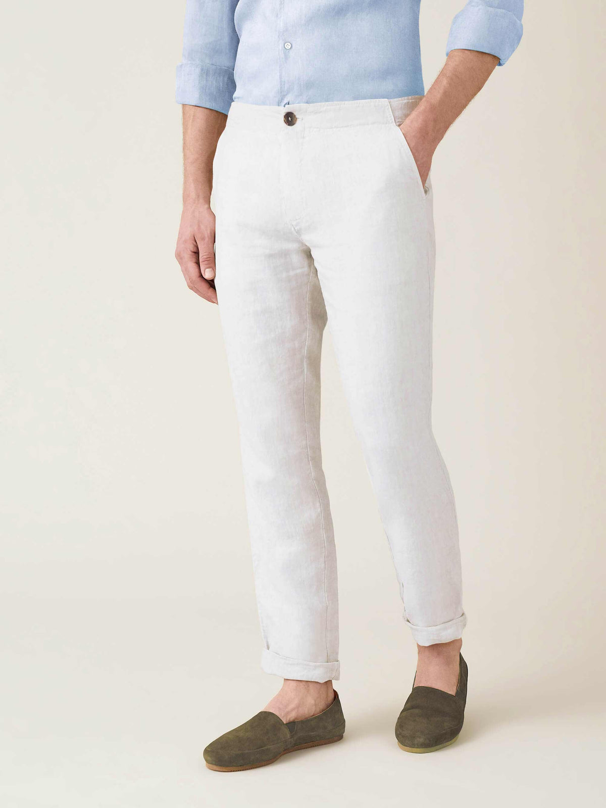 Side view of a man wearing the white Lipari linen trousers with rolled cuffs, paired with a blue shirt and green loafers.