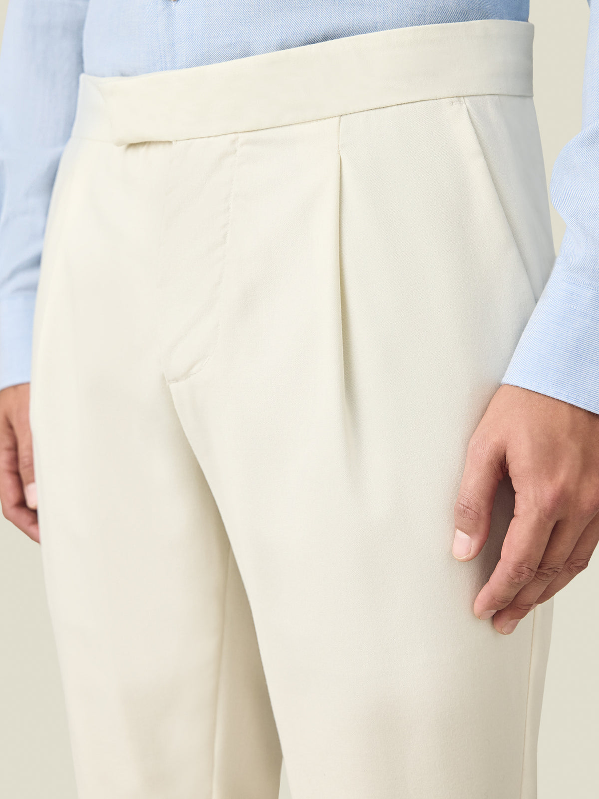 A close-up of a model wearing Luca Faloni's ivory Wool Pleated Trousers, showing the front pleat and waistband detail.