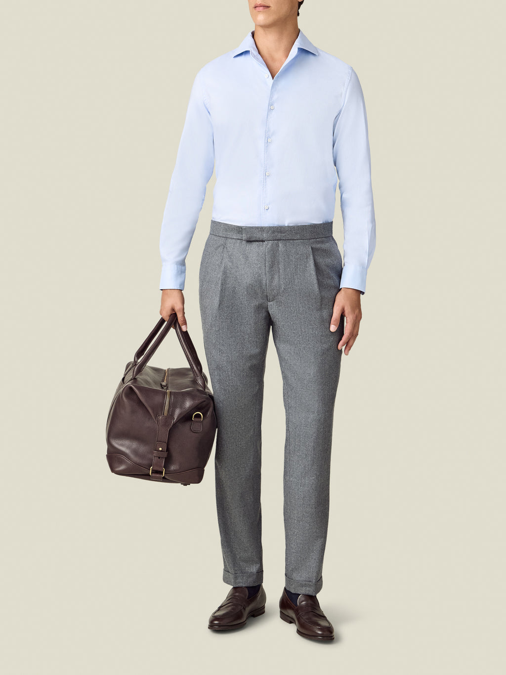 Full-body view of a model wearing the Luca Faloni light grey Wool Pleated Trousers, styled with a shirt and holding a bag.