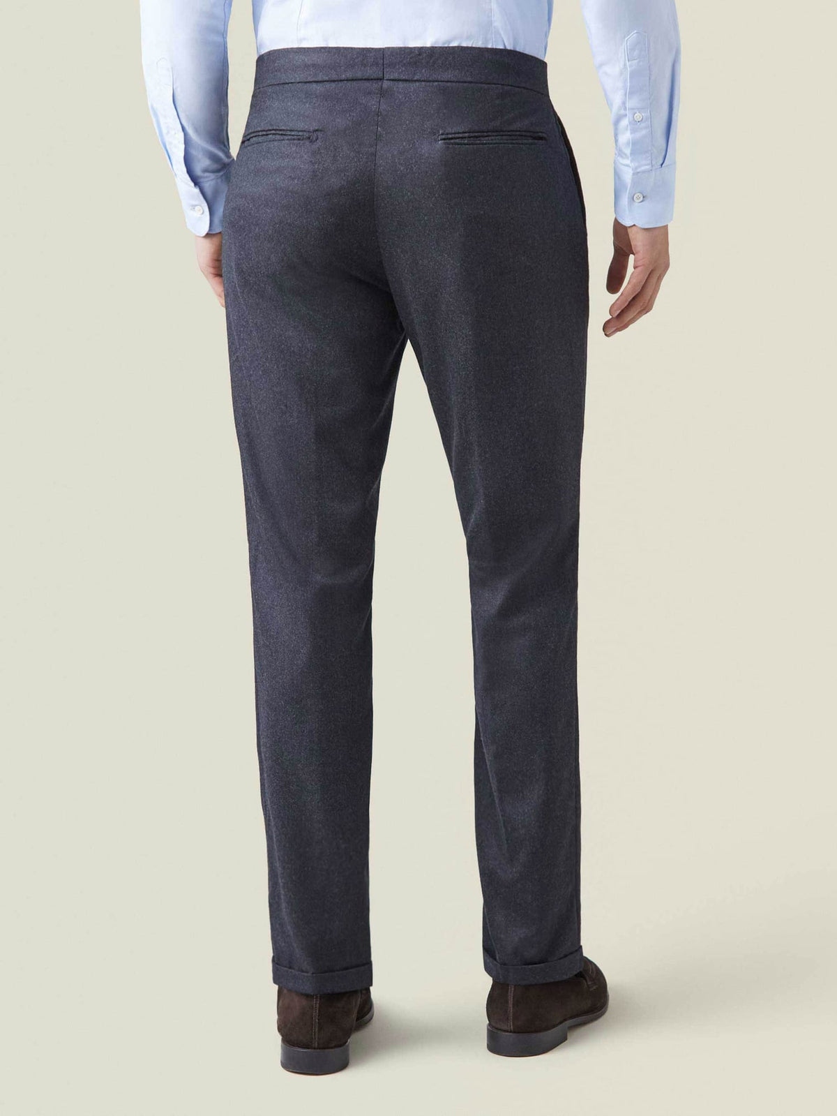 Back view of a model wearing the charcoal grey Wool Pleated Trousers, showcasing the tapered silhouette and cuffed hems.