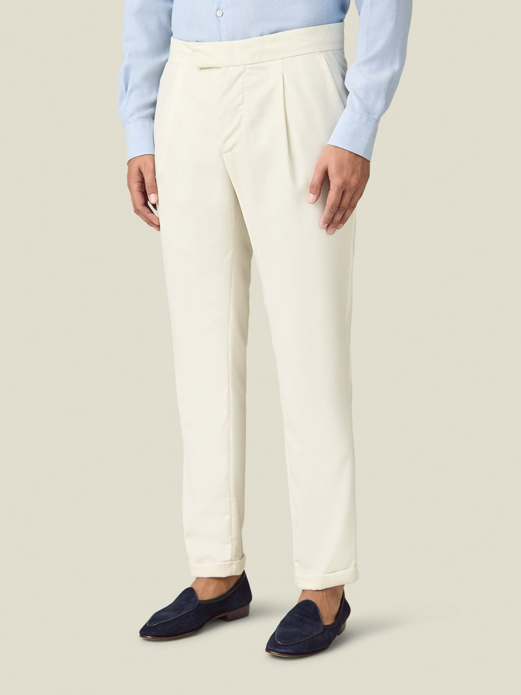 Side view of a model wearing the Luca Faloni Wool Pleated Trousers in ivory with a light blue shirt and navy loafers.