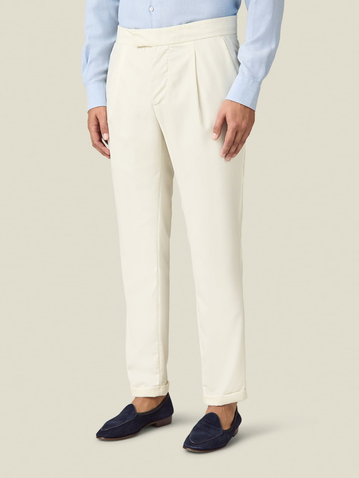 Side view of a model wearing the Luca Faloni Wool Pleated Trousers in ivory with a light blue shirt and navy loafers.