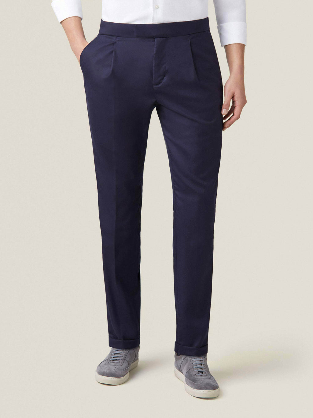 Front view of a man wearing Midnight Blue Wool Pleated Trousers with a white shirt and grey suede sneakers.
