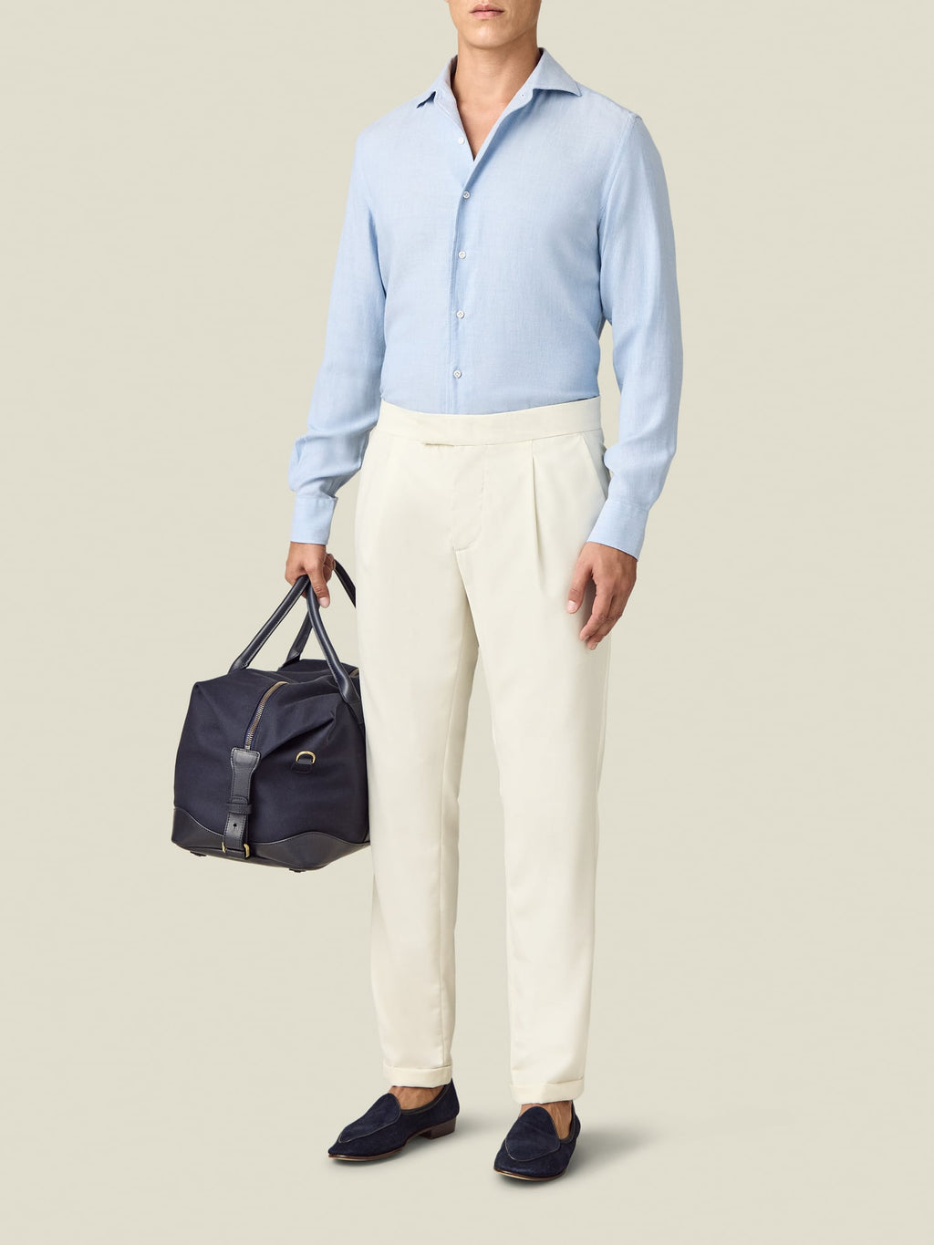 Model wearing Luca Faloni Wool Pleated Trousers in ivory with a light blue shirt and navy loafers against a plain background.