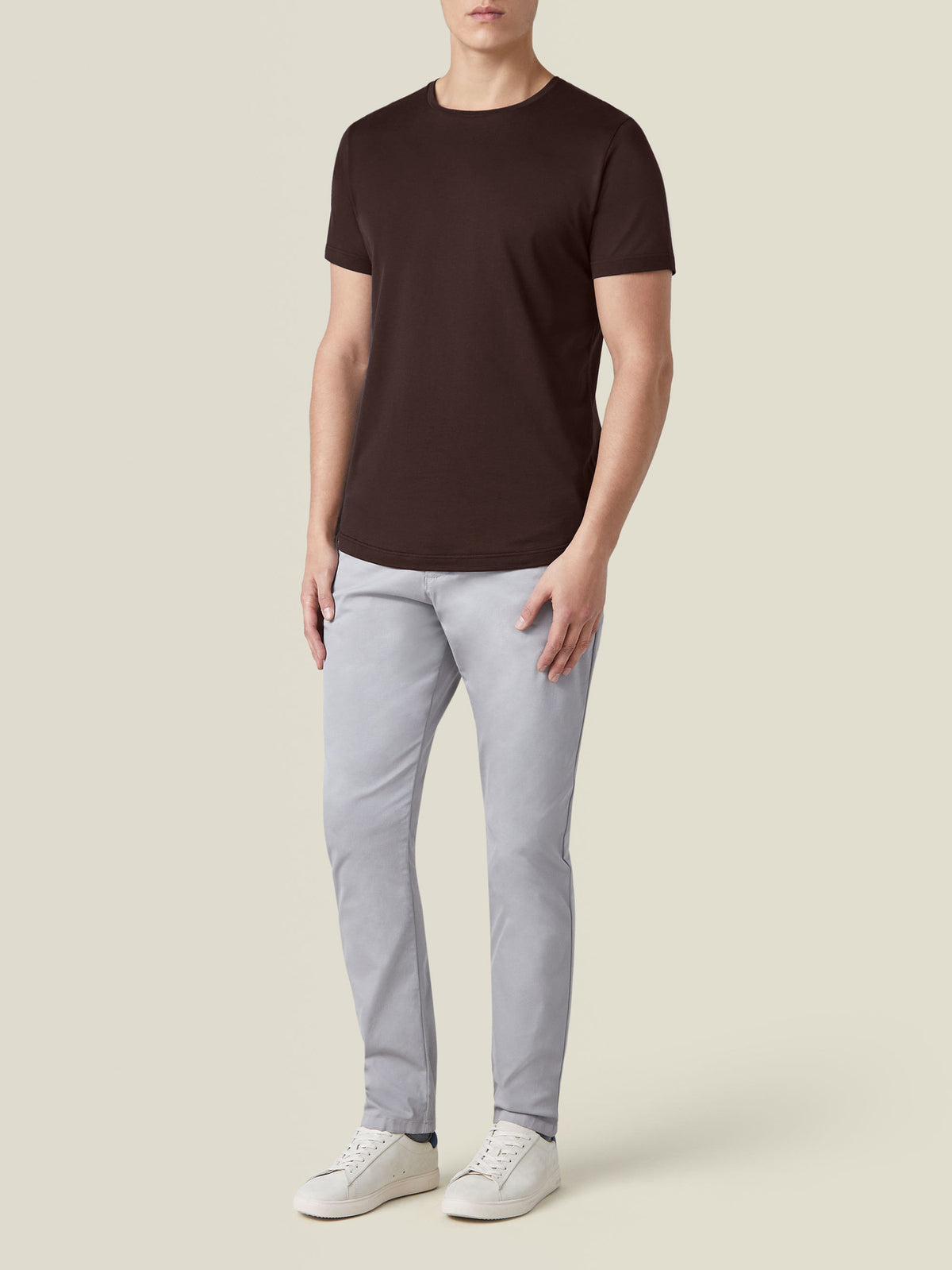 Front view of a model wearing the Silk-Cotton T-Shirt in Chocolate Brown, paired with light grey trousers and white sneakers.