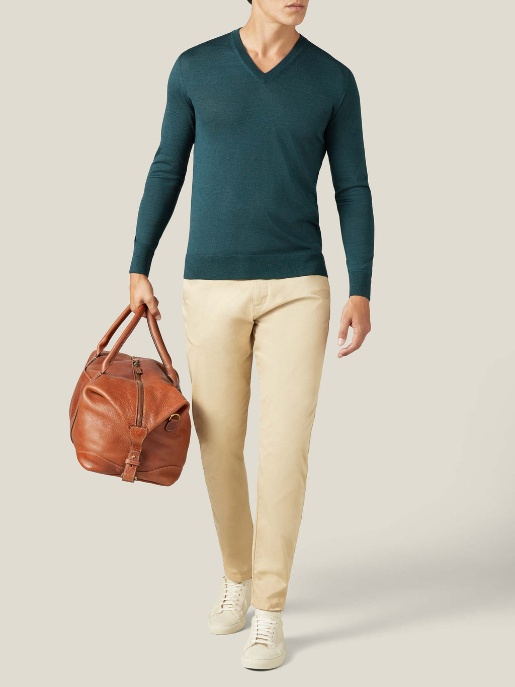 A man models the Luca Faloni Silk-Cashmere V-neck in Forest Green, styled with beige trousers and carrying a leather bag.
