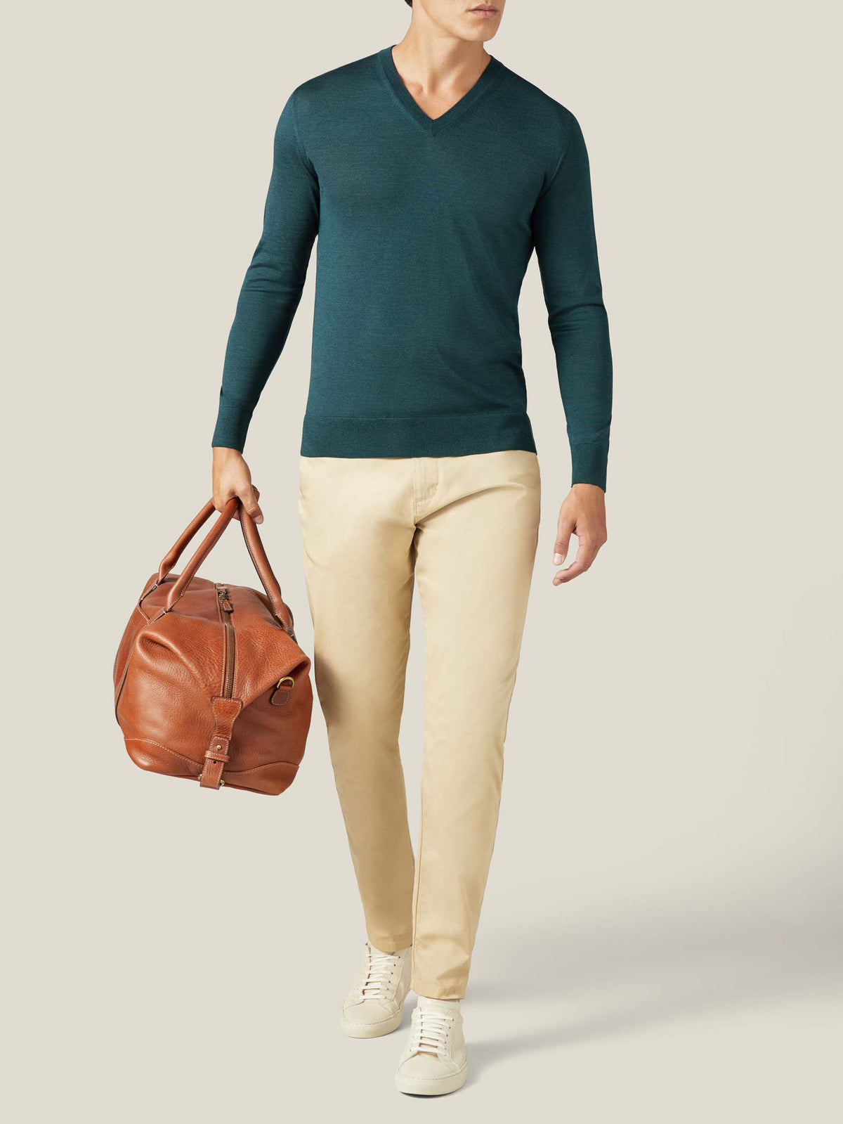 A man models the Luca Faloni Silk-Cashmere V-neck in Forest Green, styled with beige trousers and carrying a leather bag.