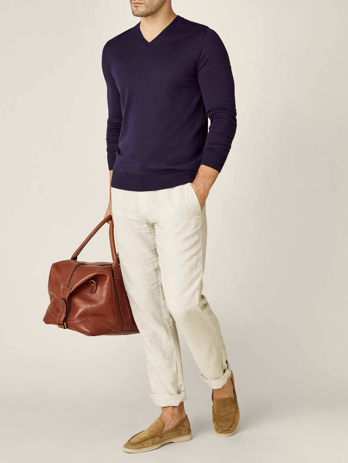 A model wears the Navy Blue Silk-Cashmere V-Neck, styled with cream trousers, suede loafers, and a leather weekend bag.