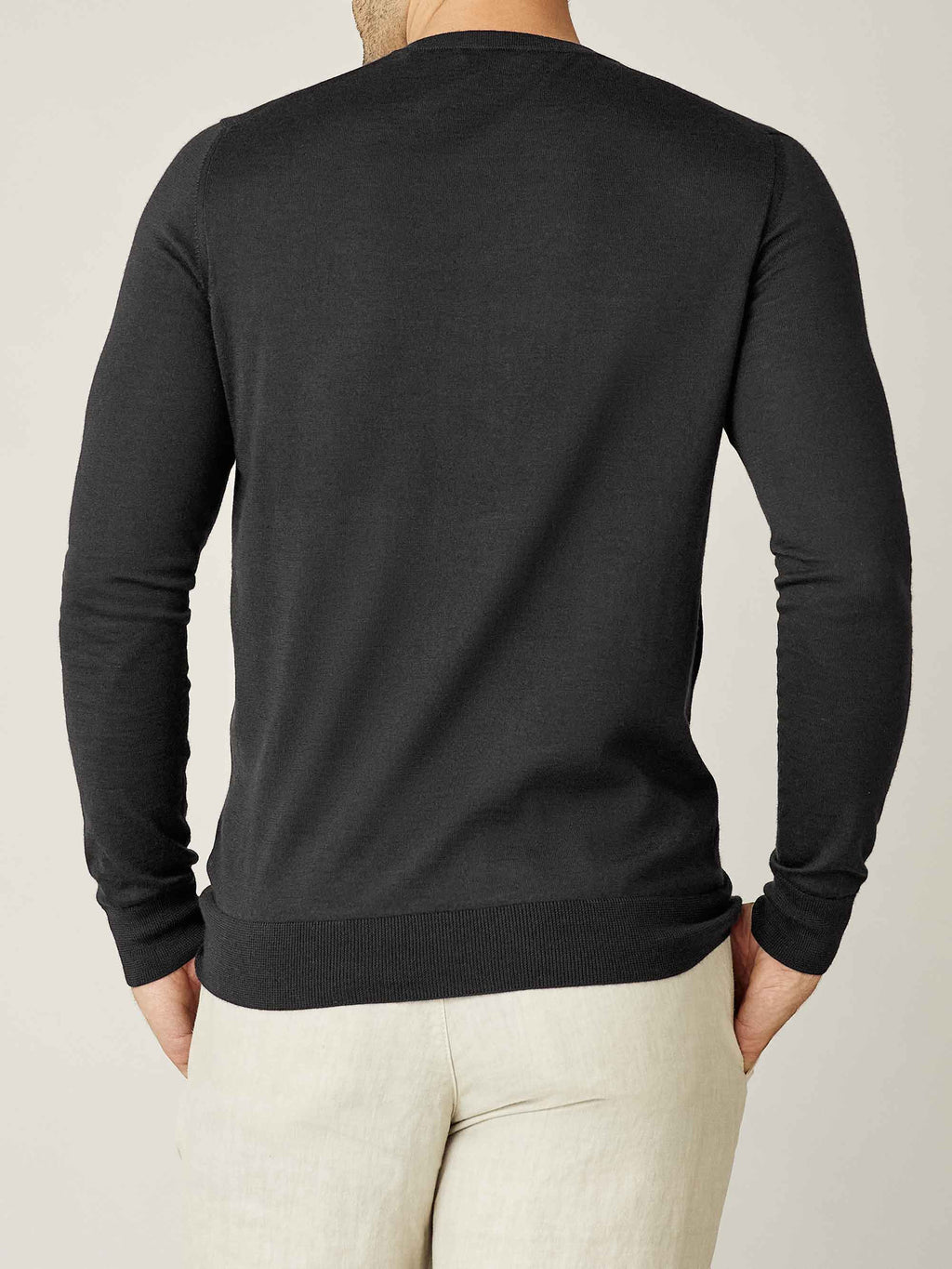 Back of a model wearing the charcoal grey silk-cashmere V-neck sweater with light coloured trousers.
