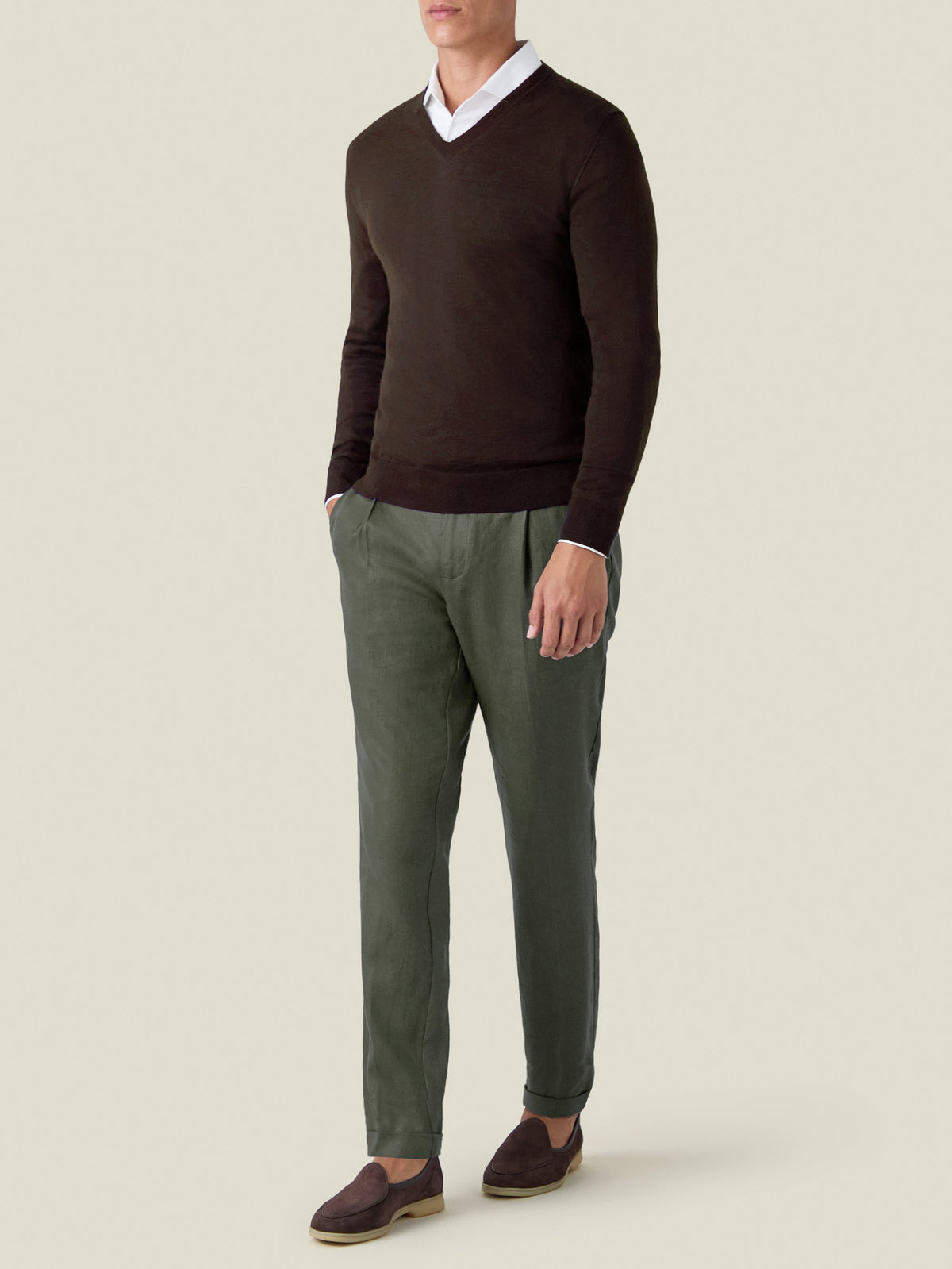 A man models the Luca Faloni chocolate brown silk-cashmere V-neck layered over a white shirt with olive green trousers.