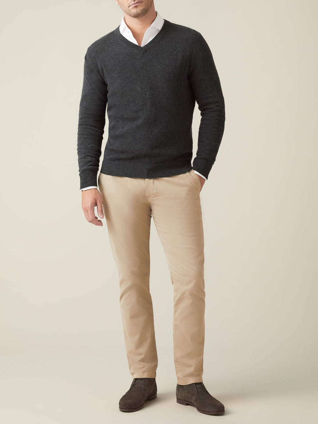 A model wears the Luca Faloni charcoal grey cashmere V-neck sweater layered over a white shirt with beige chinos.
