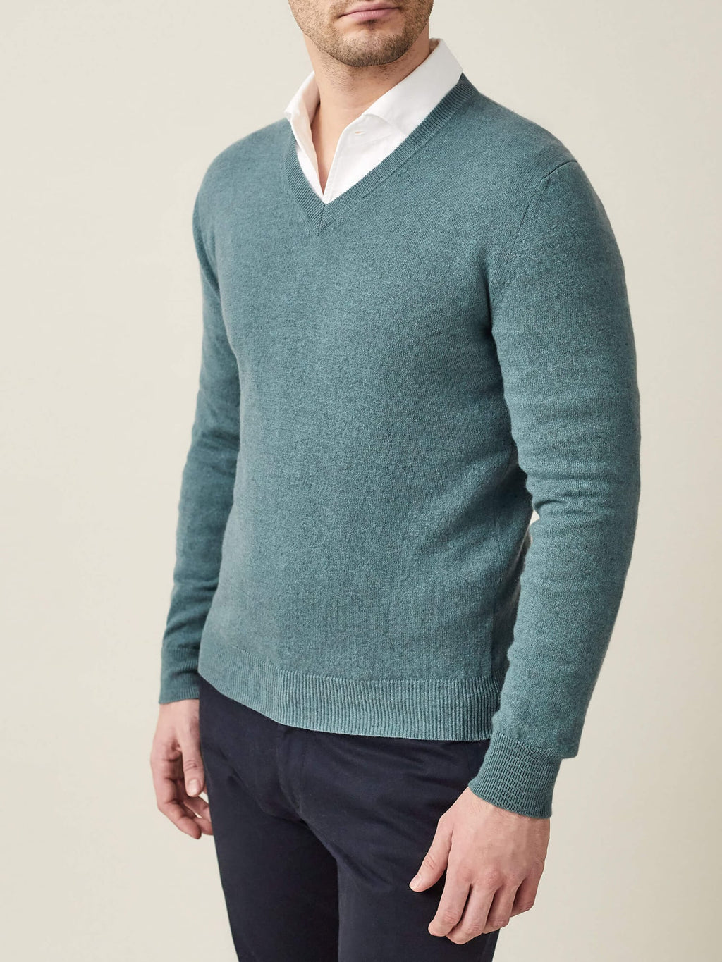 Model wears the Luca Faloni V Neck in marine green cashmere, styled over a white shirt with dark trousers.