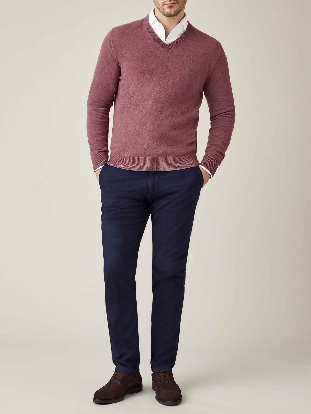 Model wears Luca Faloni's Desert Rose cashmere v-neck over a white shirt with dark blue trousers against a plain background.