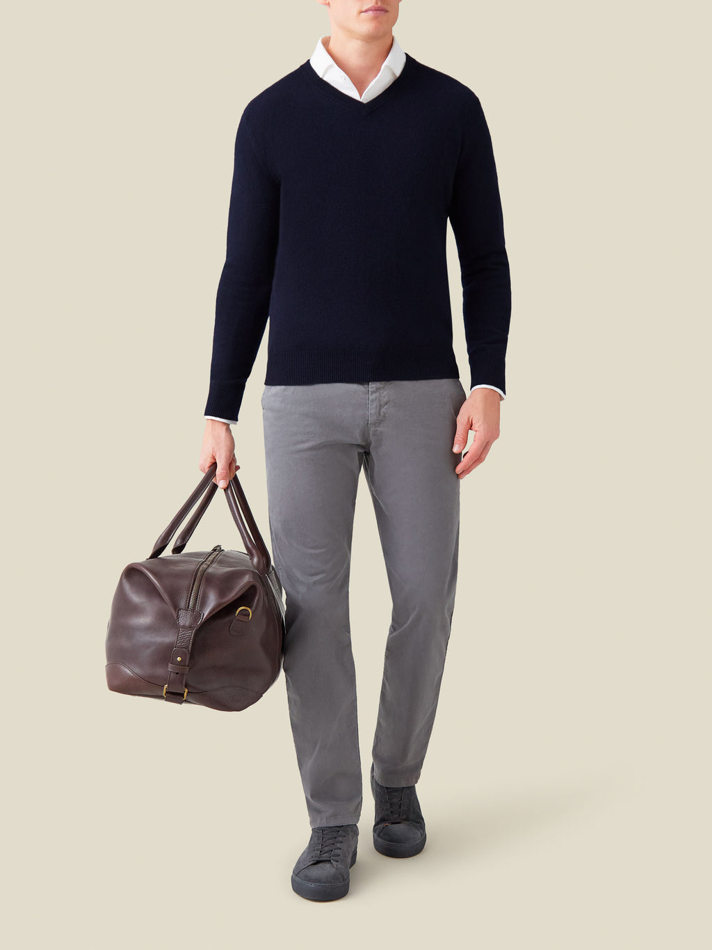 Man wears the Midnight Blue Cashmere V Neck over a white shirt, paired with grey trousers and holding a brown leather bag.