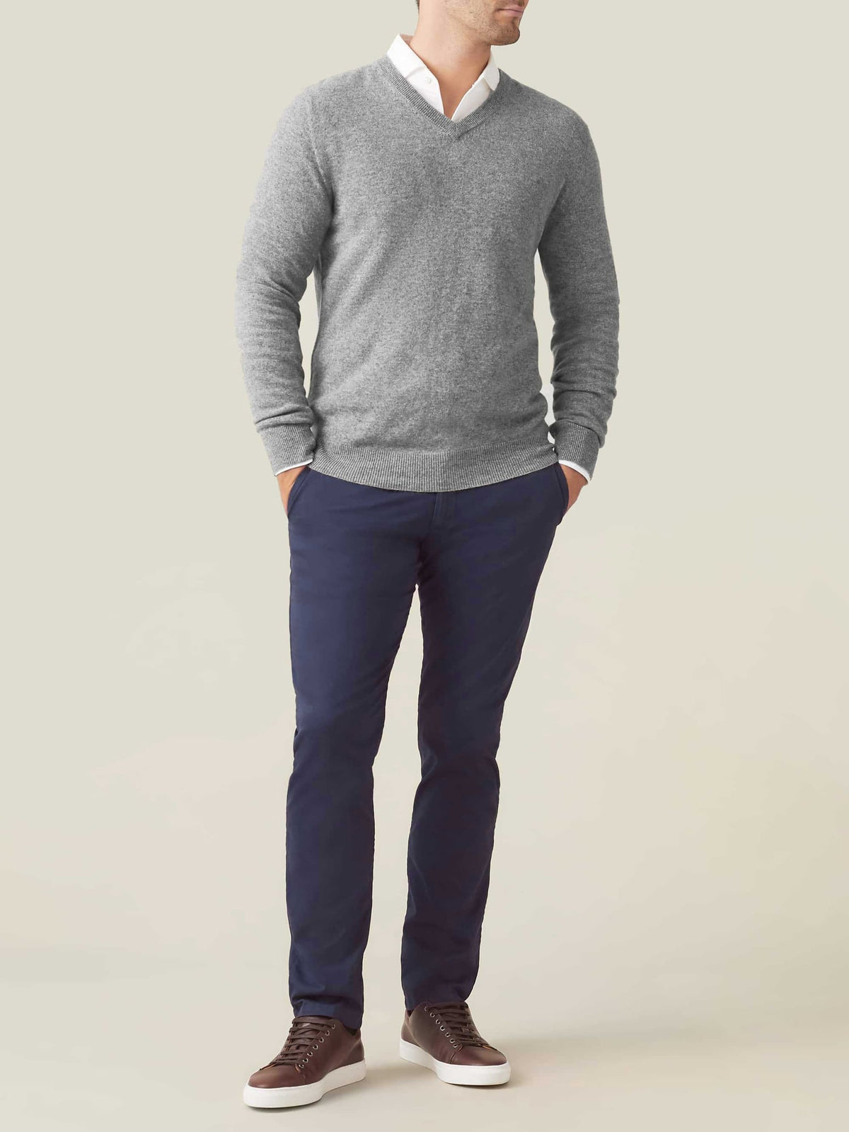Full view of a man wearing the Dolomiti Grey cashmere V-neck jumper, styled with a white shirt, navy trousers and trainers.