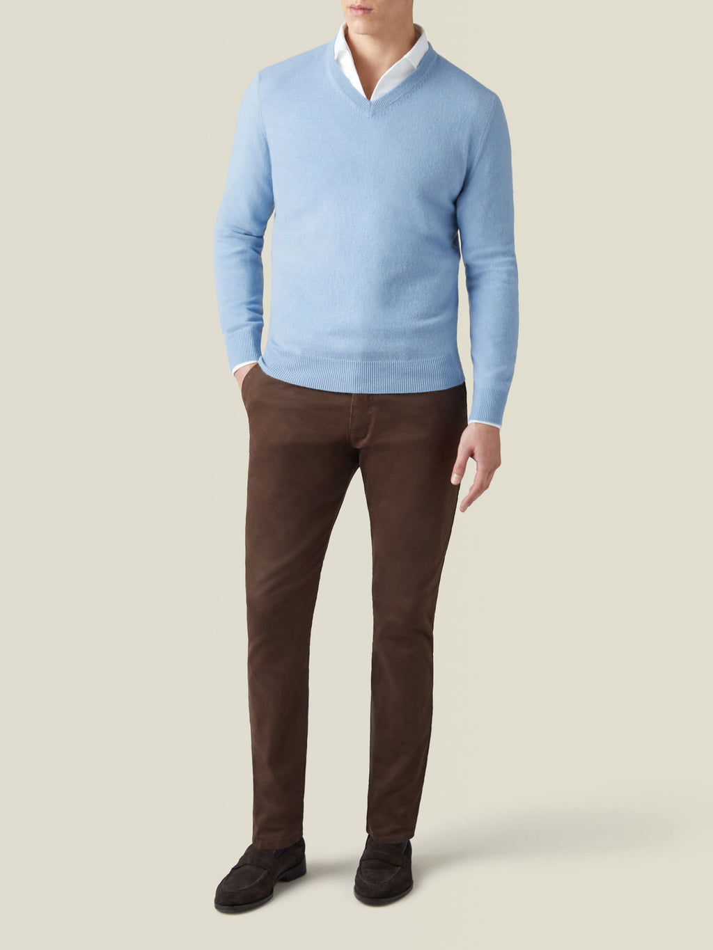 Full-length shot of a model wearing the sky blue cashmere V-neck jumper with a white shirt and brown trousers.