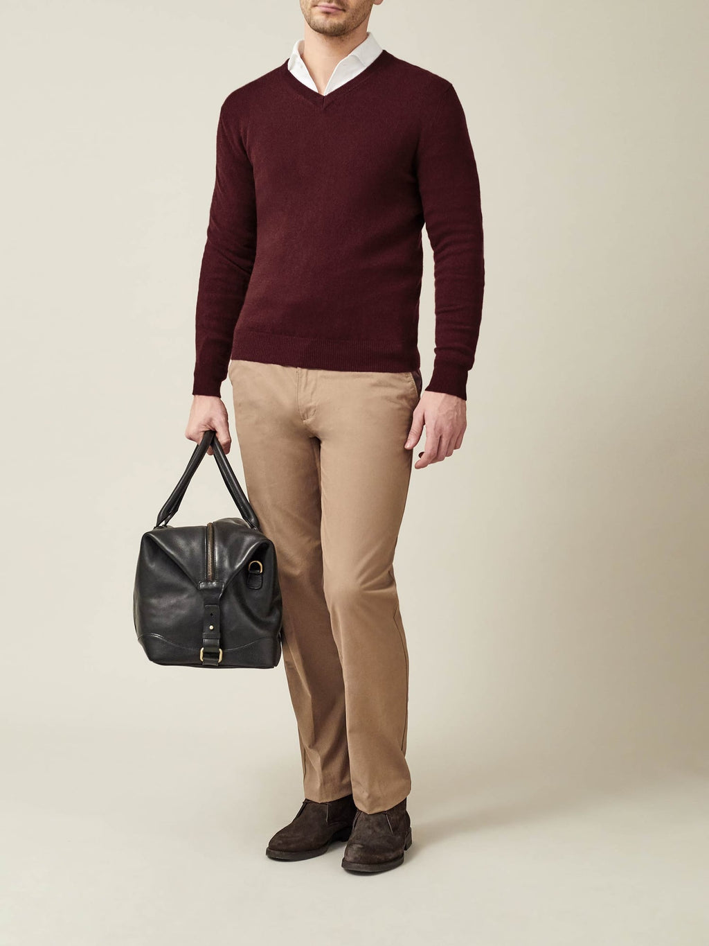 Model wears a lava red cashmere V-neck jumper over a white shirt with beige chinos, holding a black bag.