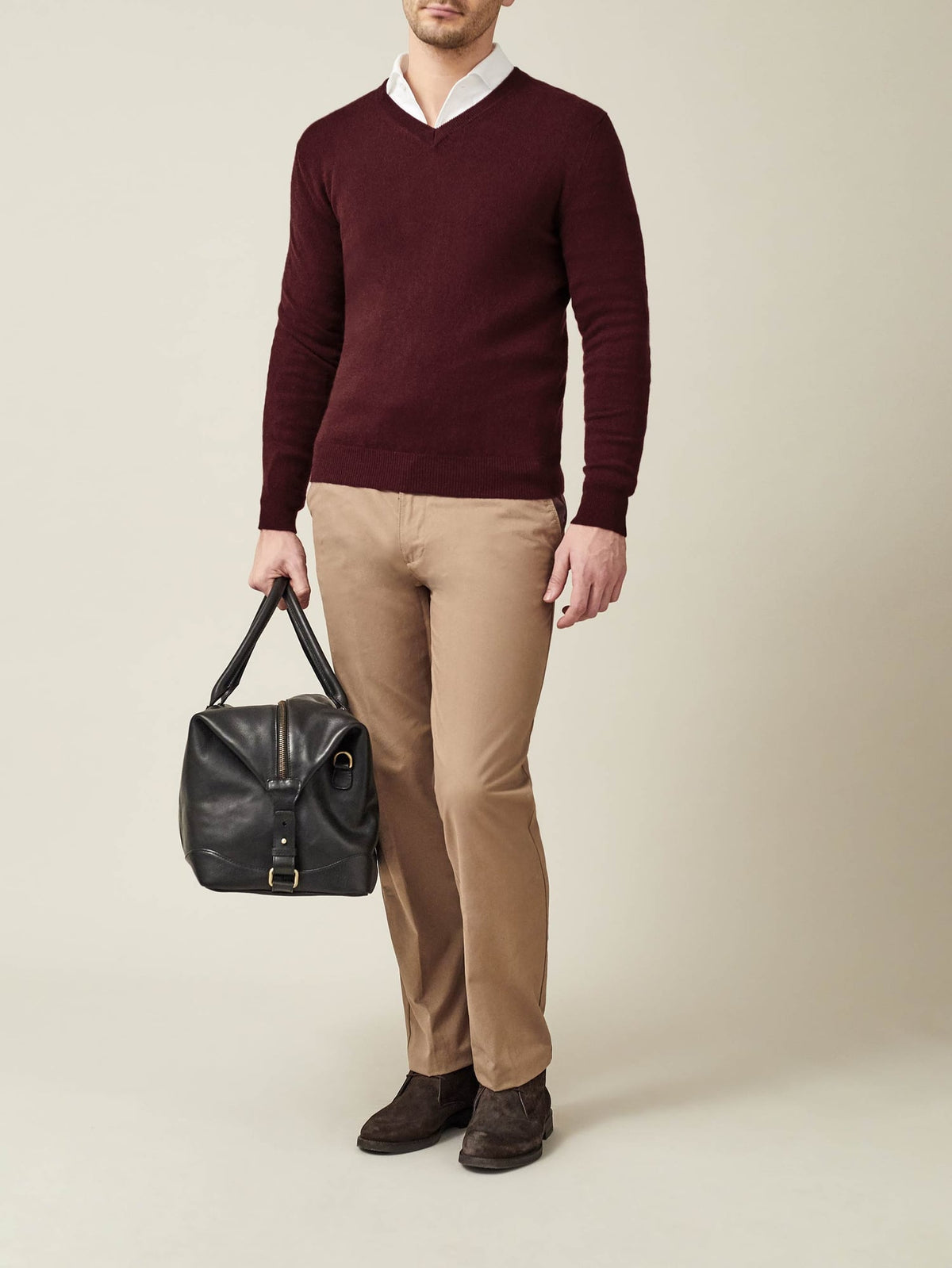 Model wears a lava red cashmere V-neck jumper over a white shirt with beige chinos, holding a black bag.