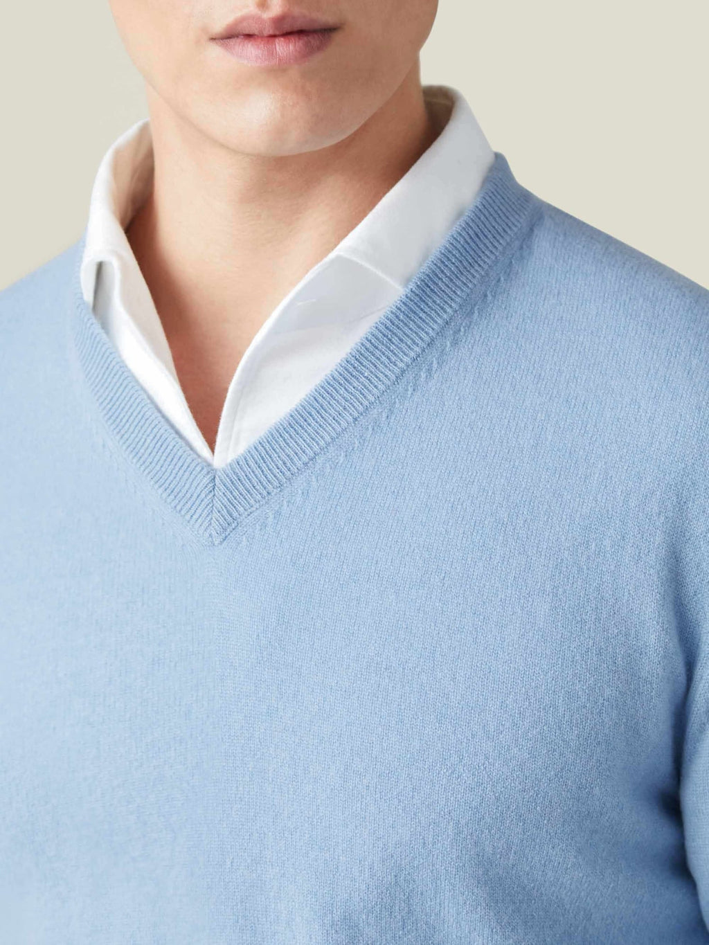Close-up of a man wearing a sky blue cashmere V-neck sweater layered over a white collared shirt, showing the neckline.