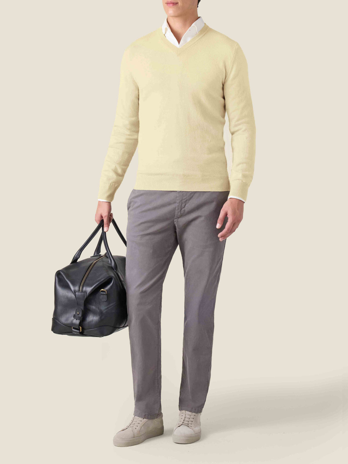 Model wears the yellow pure cashmere V-neck sweater layered over a white shirt, with grey trousers and a black leather bag.