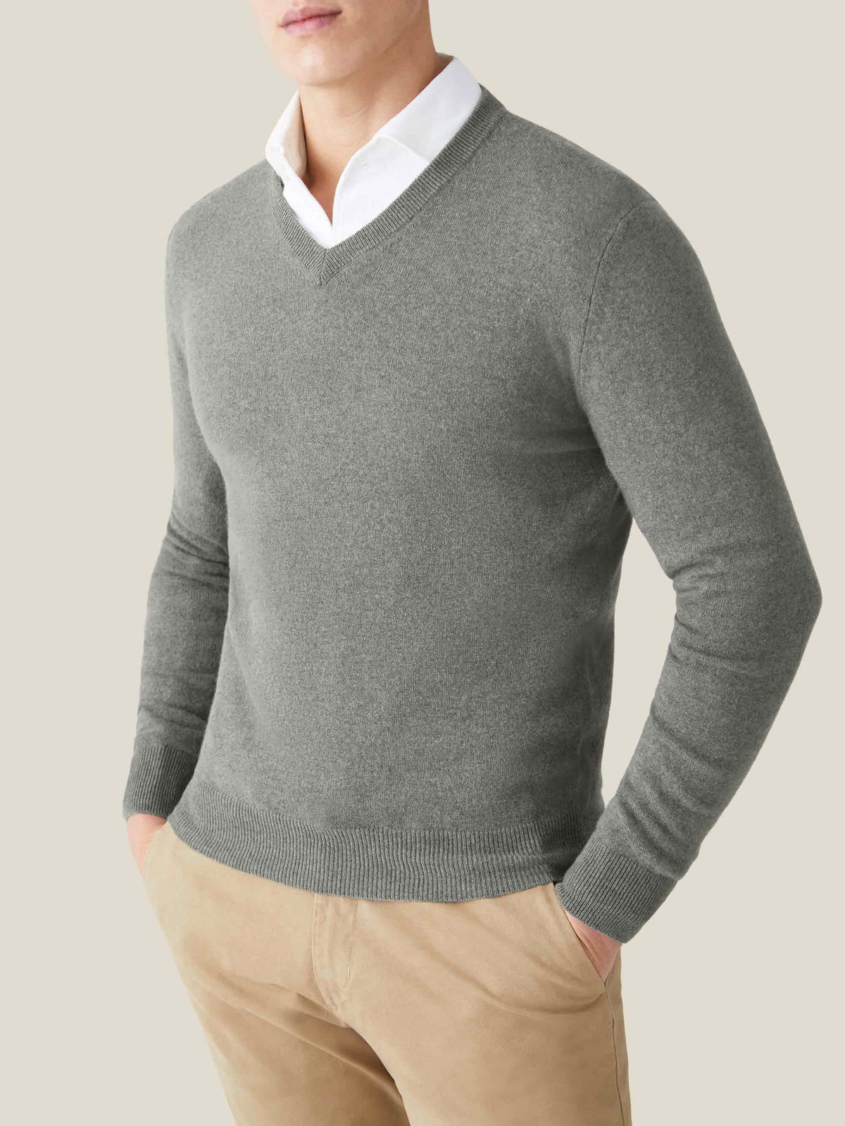 Model from the chest up wearing a moss green cashmere v-neck sweater over a white collared shirt and beige chinos.