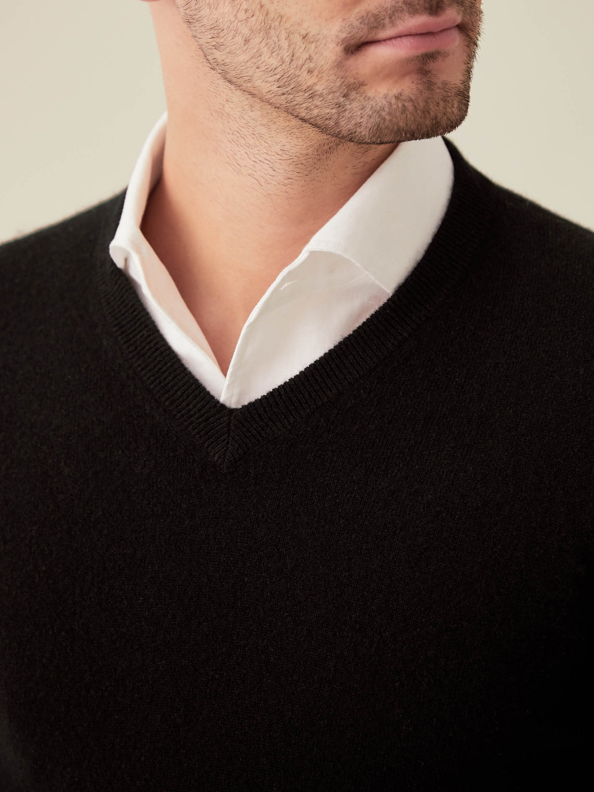 A close-up shot of a man wearing a black cashmere V-neck sweater layered over a classic white shirt.