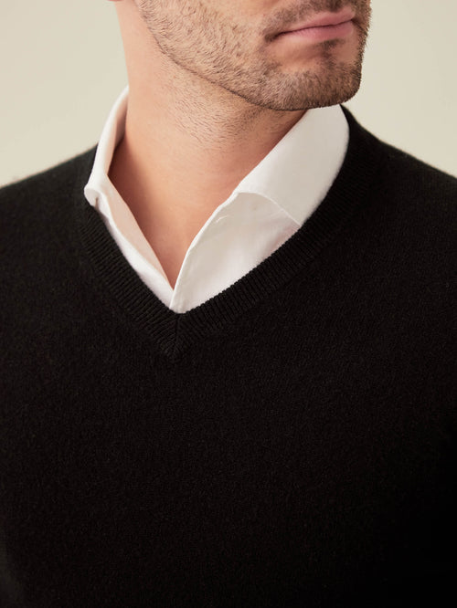 A close-up shot of a man wearing a black cashmere V-neck sweater layered over a classic white shirt.