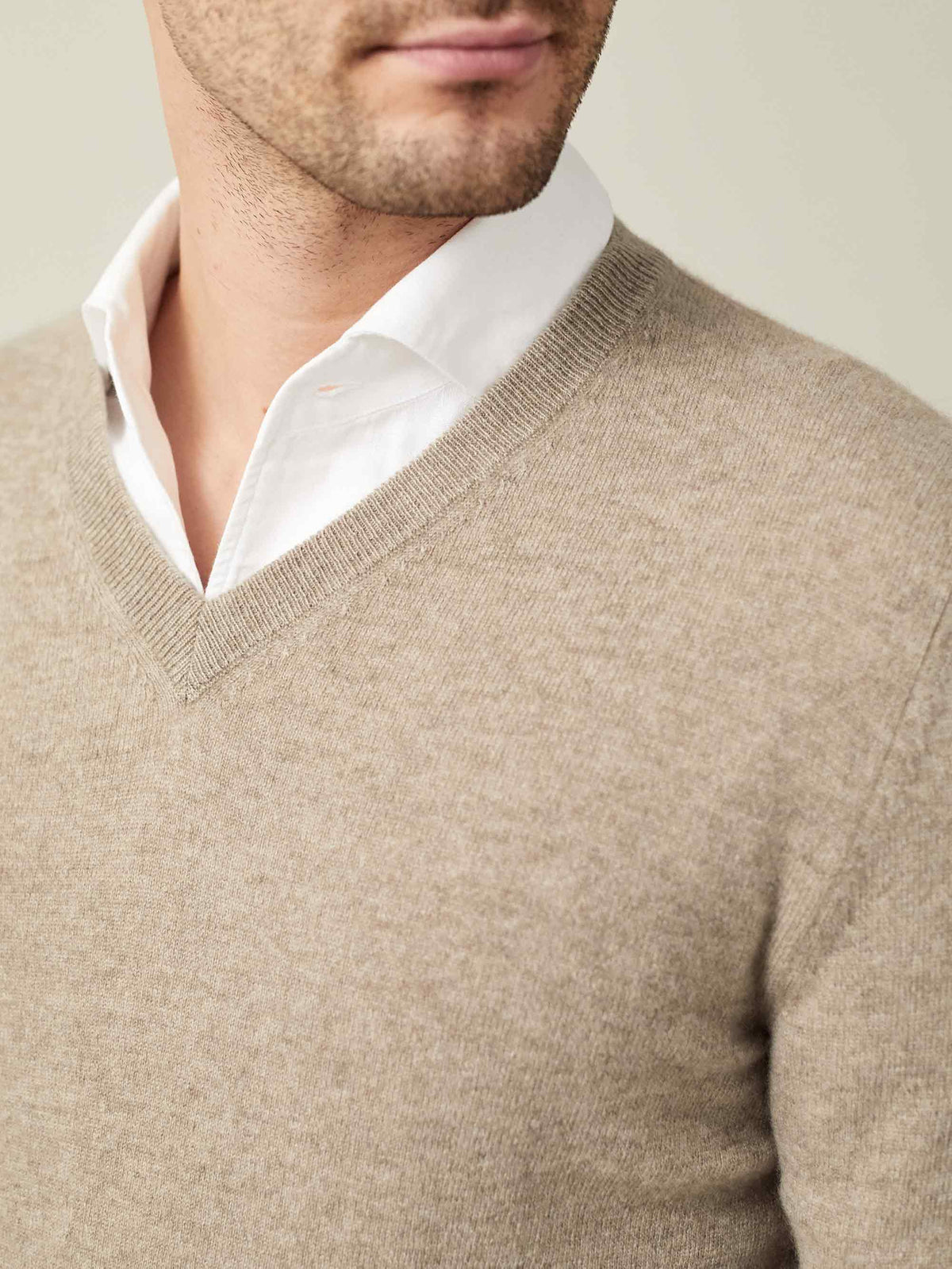 Close-up detail of a man wearing a camel beige cashmere V-neck sweater over a white shirt, showcasing the ribbed neckline.